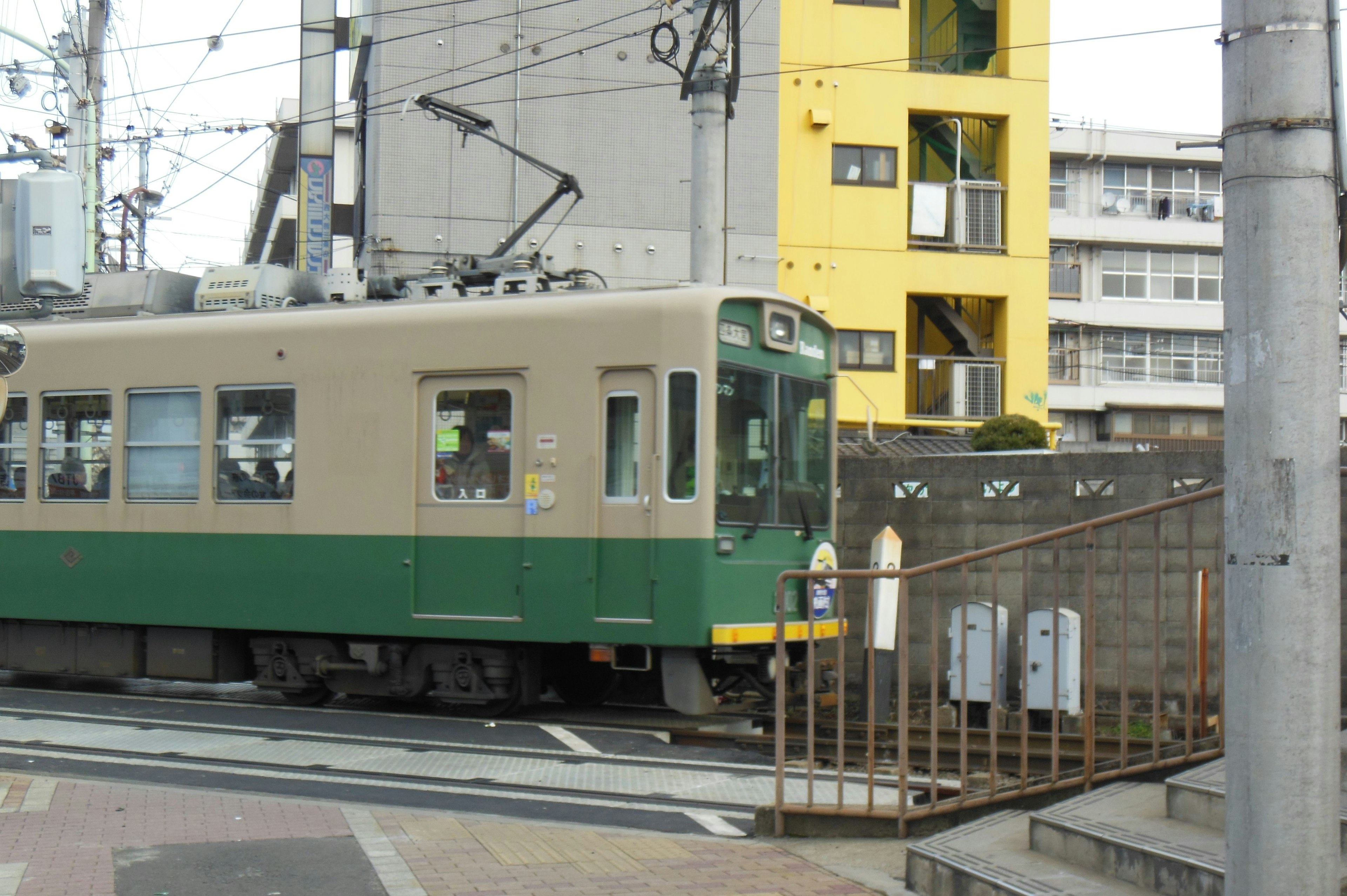 Eine grüne Straßenbahn, die an einem gelben Gebäude vorbeifährt