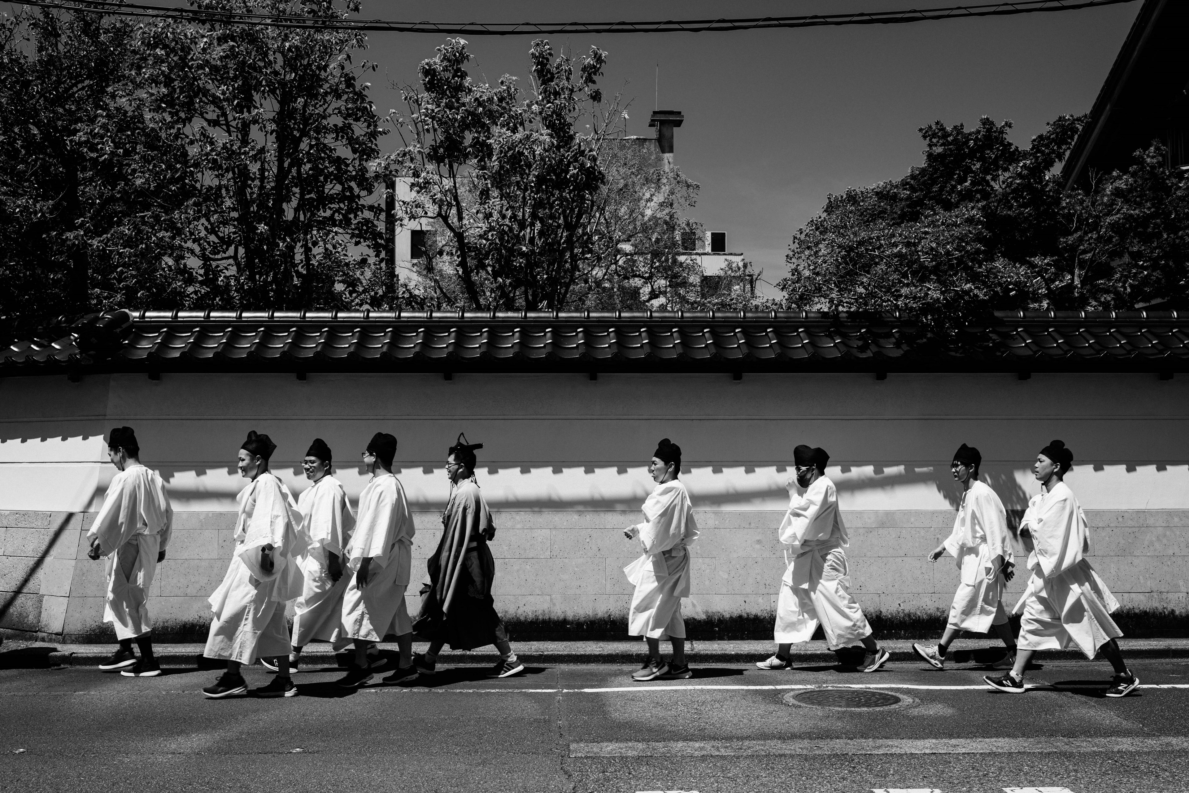 Black and white photo of people in white garments walking along a traditional street