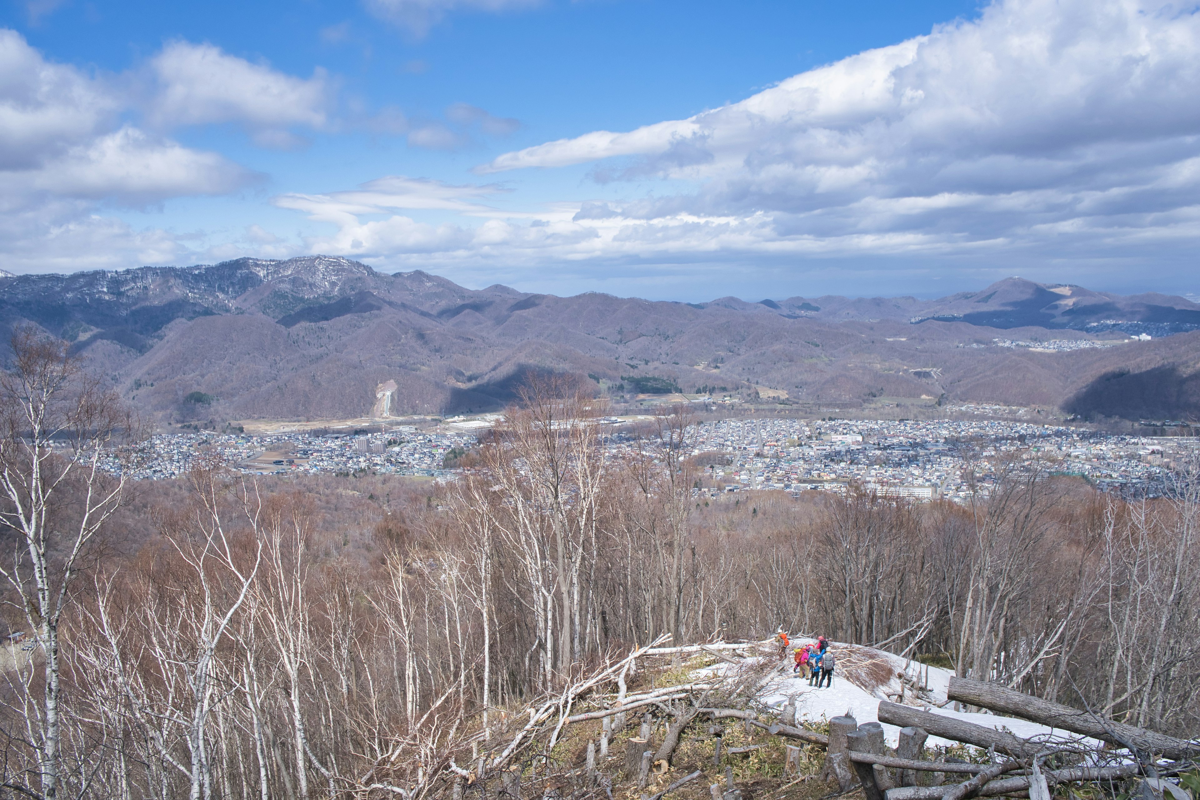 Vue panoramique depuis un sommet de montagne montrant des paysages d'hiver et une ville en contrebas sous un ciel bleu avec des nuages blancs