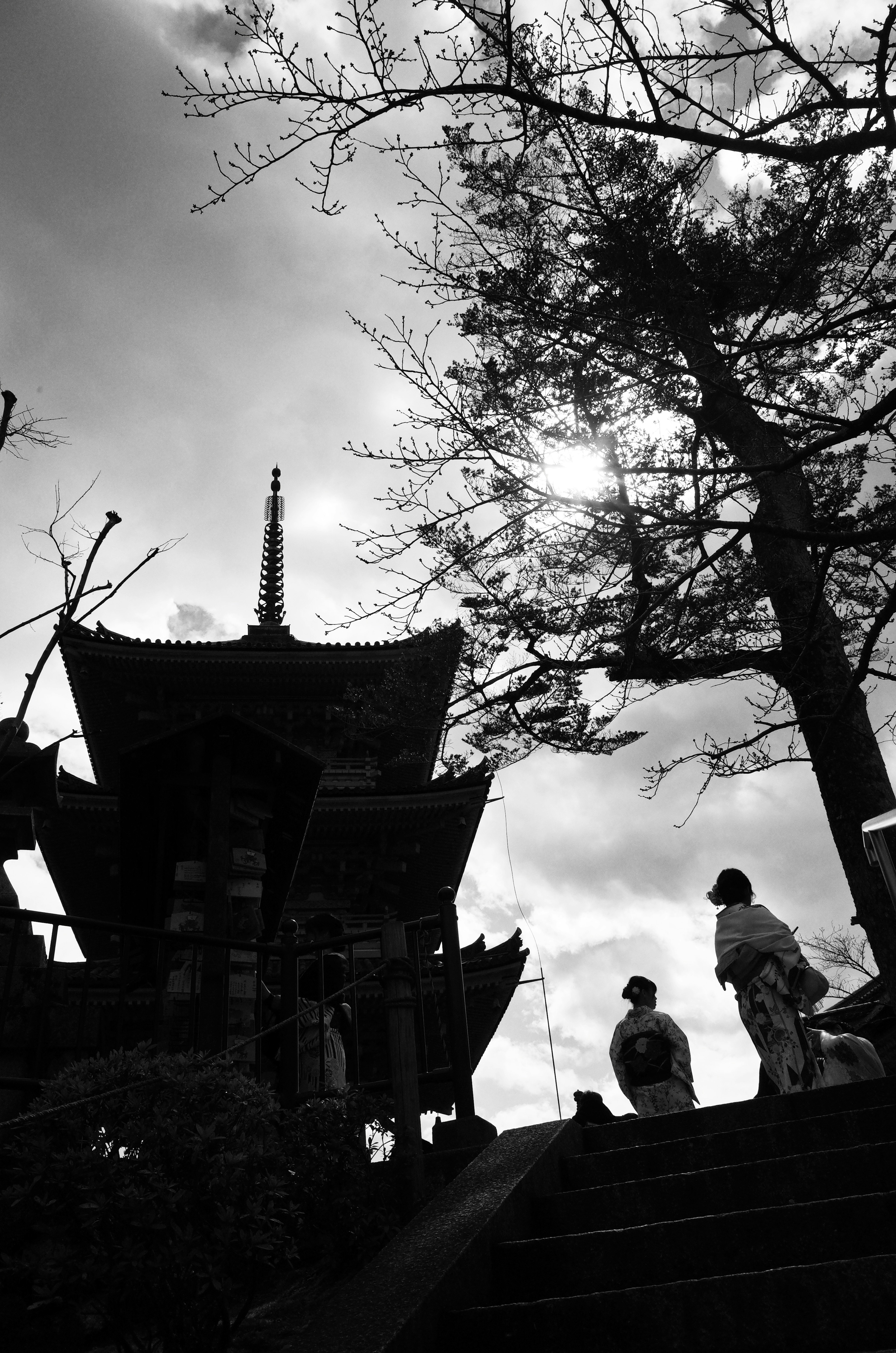 Silueta de una pagoda con figuras y un árbol contra un cielo nublado