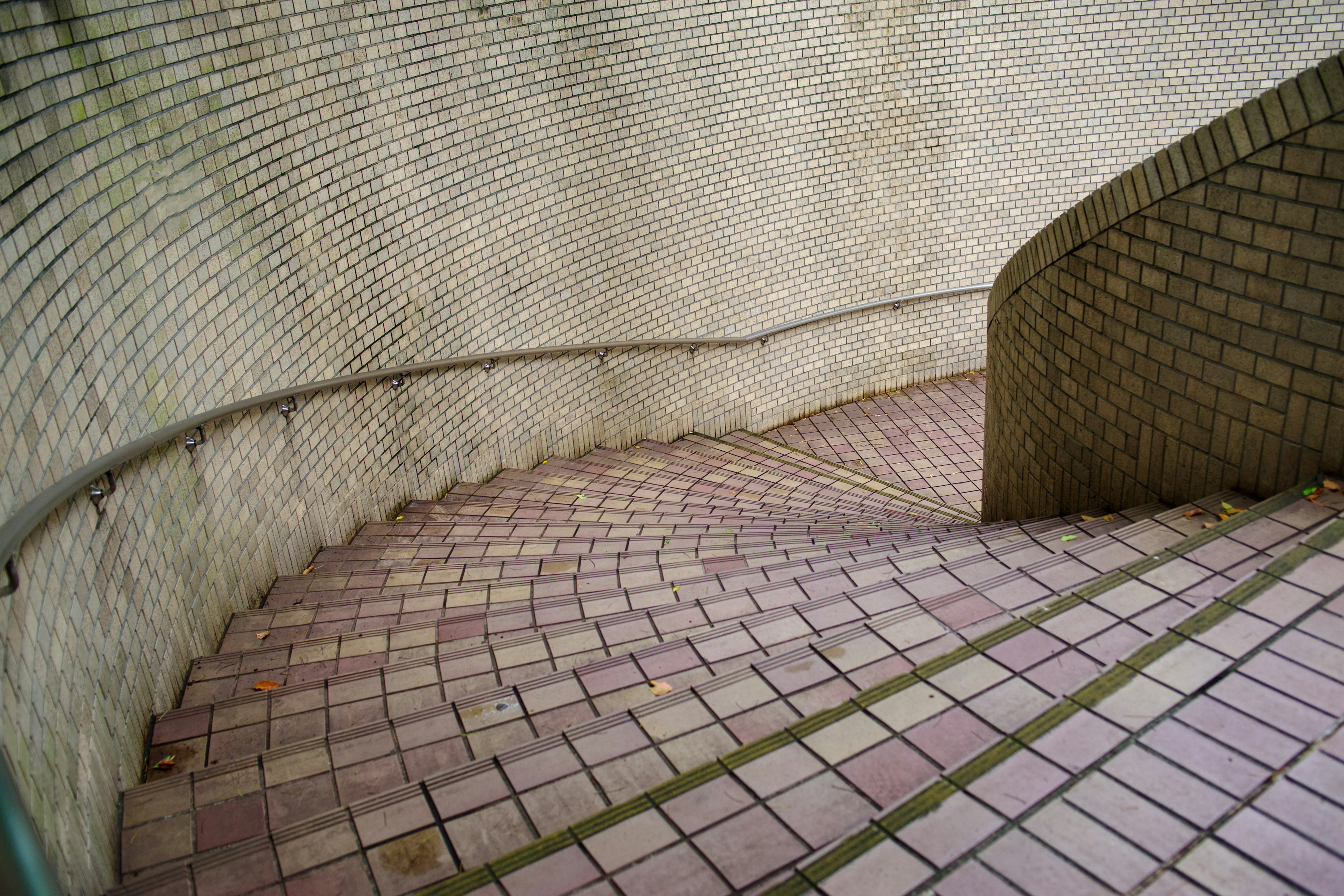 Escalier en colimaçon descendant avec des murs en briques et un sol carrelé