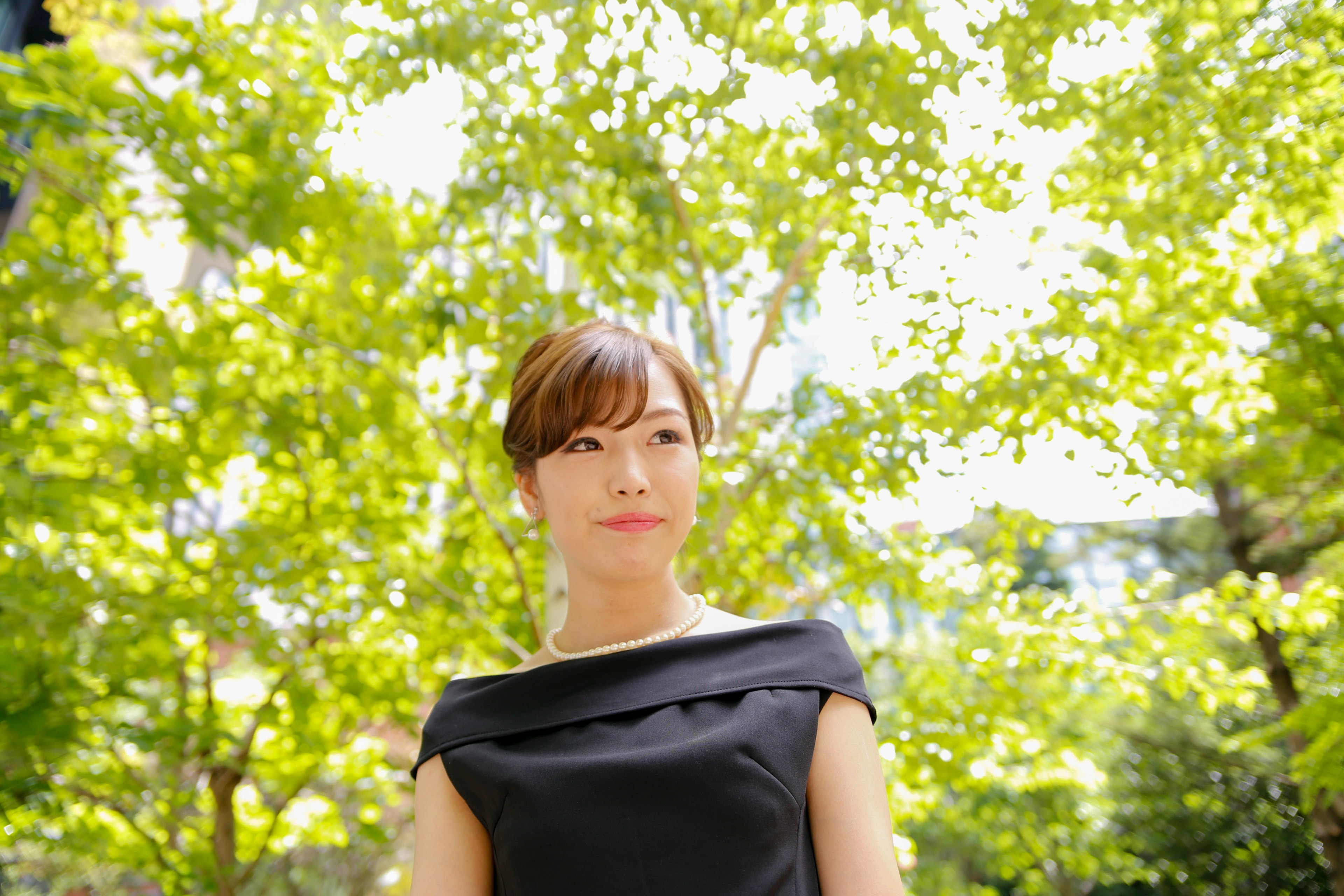 Portrait of a woman standing amidst green trees wearing a black dress