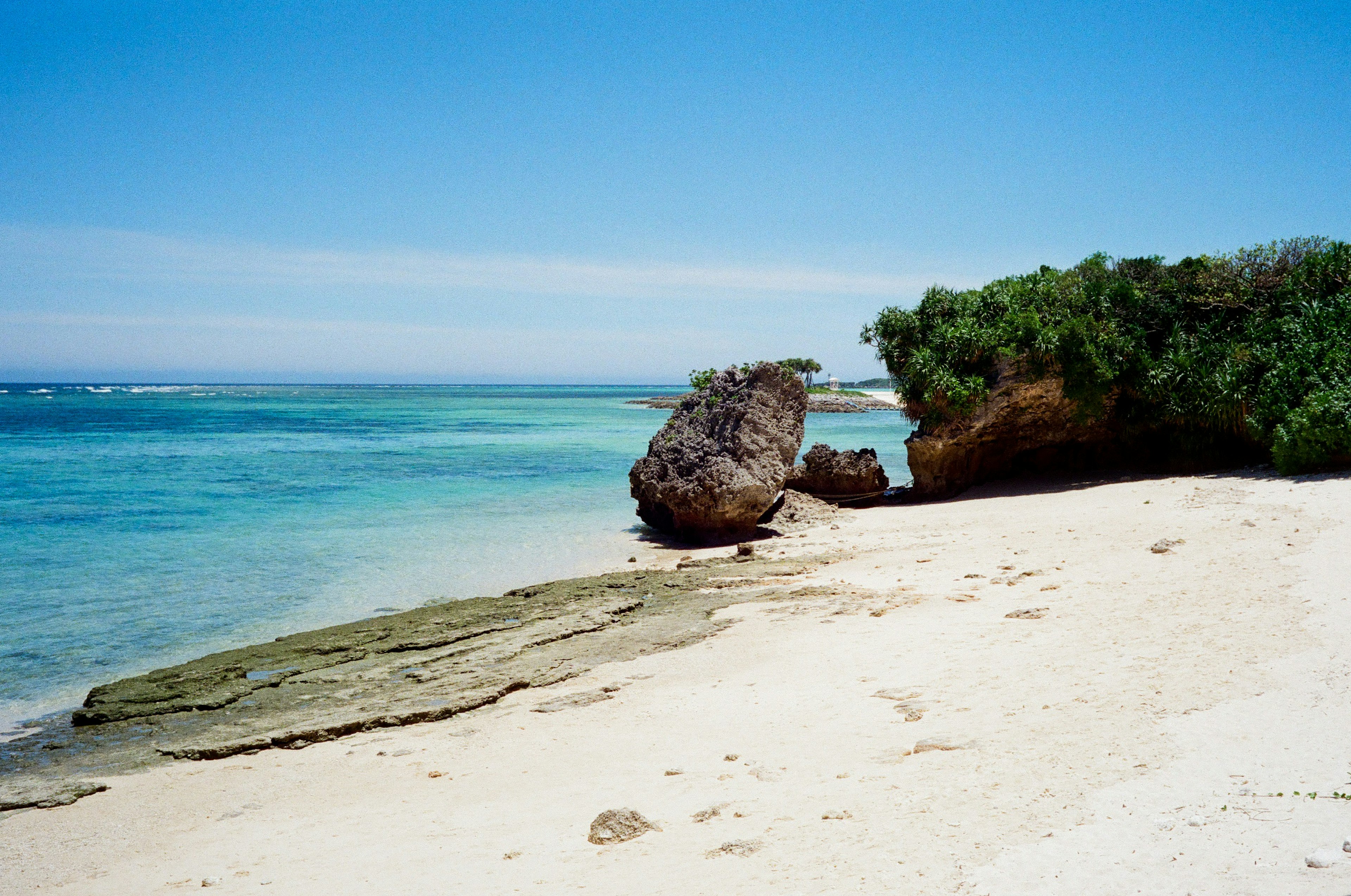 Vista escénica del océano azul y la playa de arena blanca con una gran roca y vegetación verde