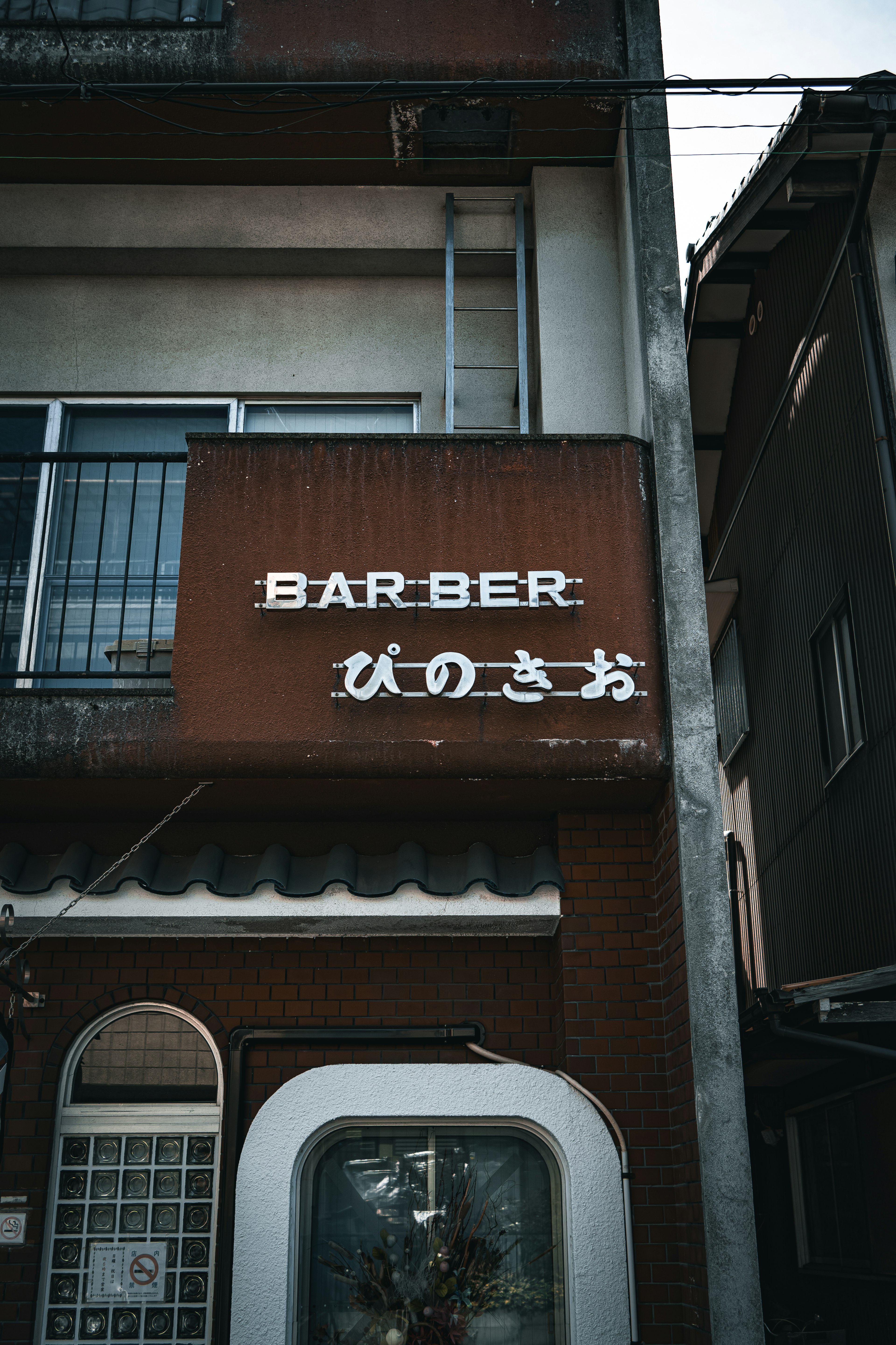 一棟老建築的外觀，上面有日語和英語的BARBER標誌