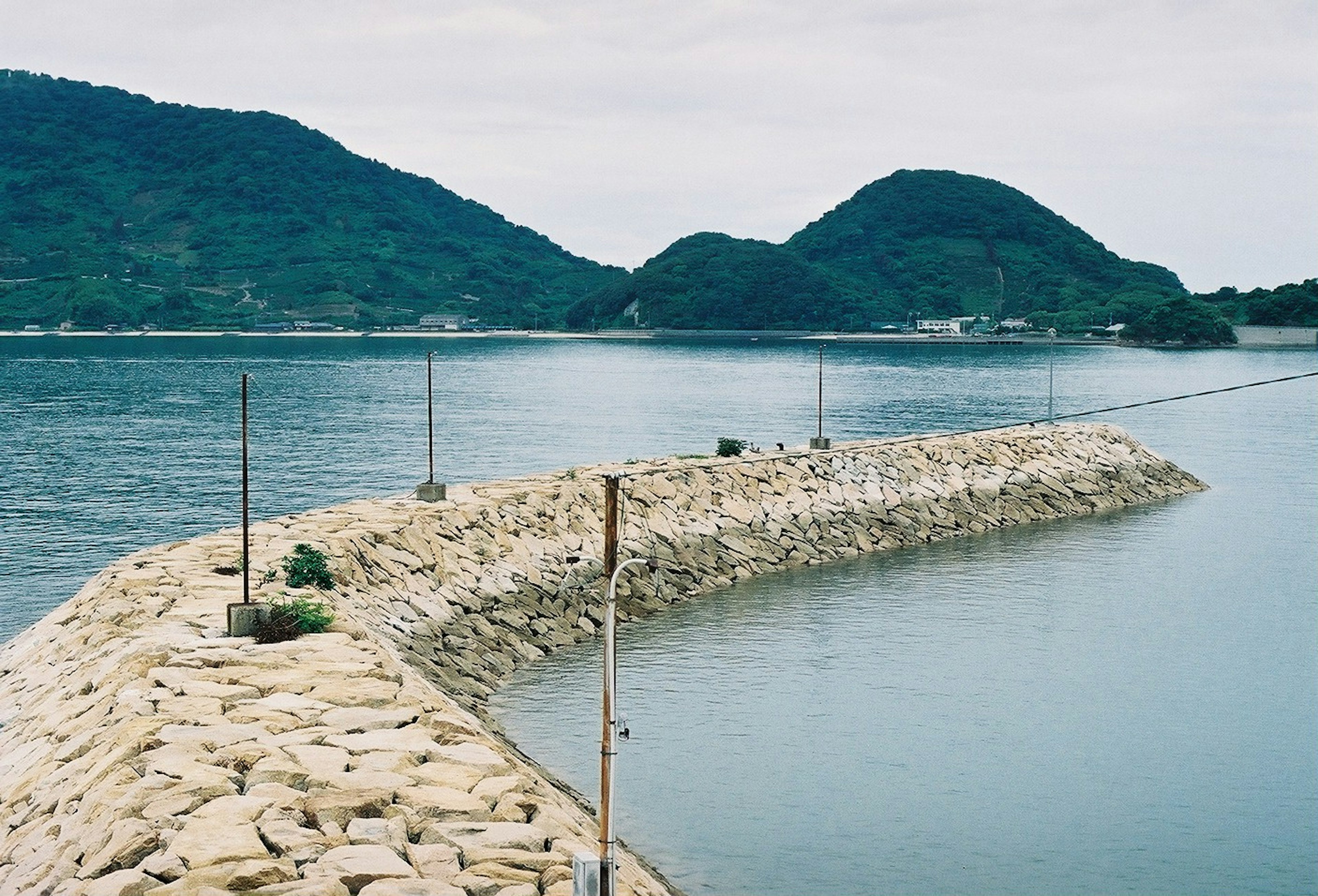 Stone breakwater in a calm sea with green hills in the background