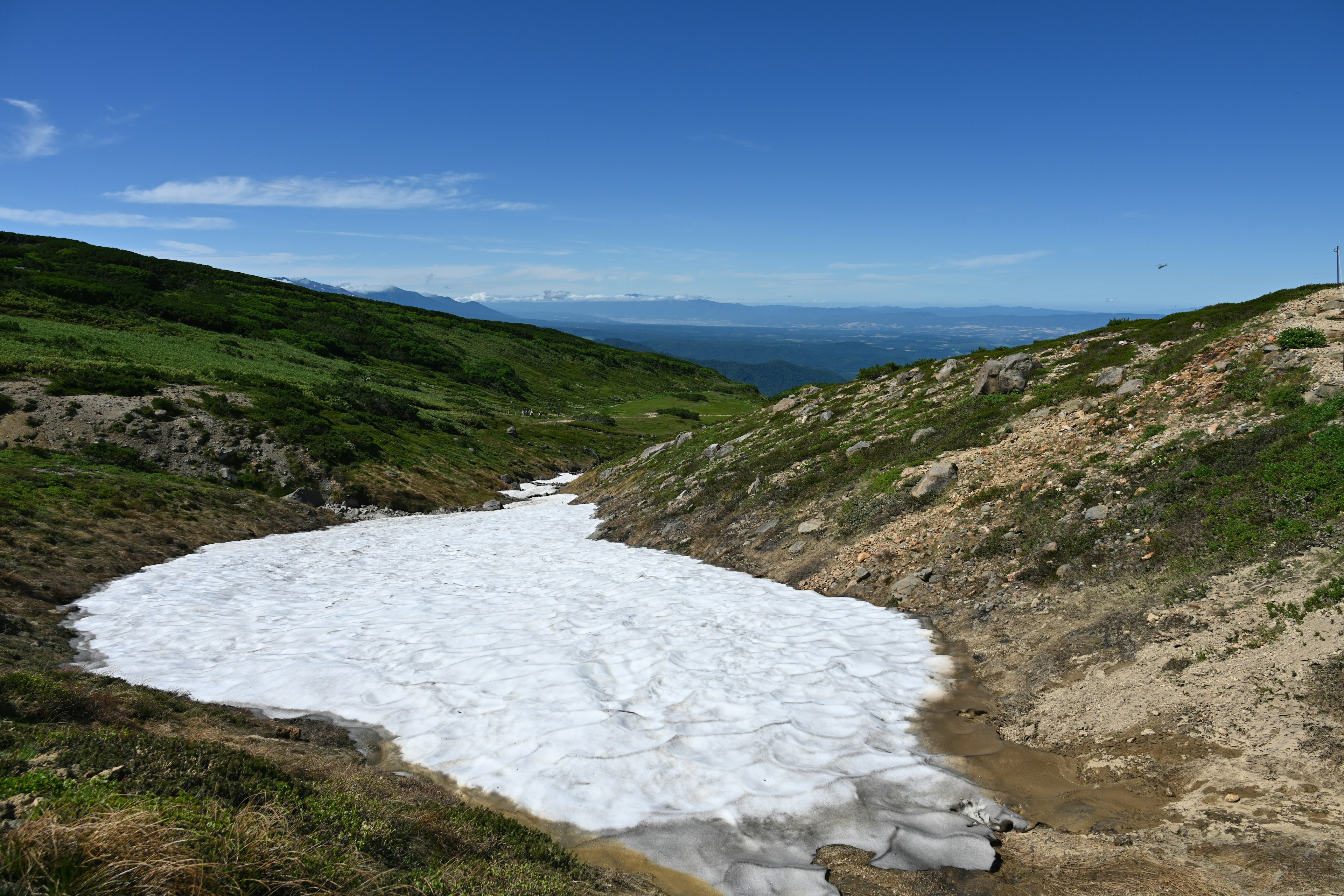 Parche de nieve en una colina cubierta de hierba bajo un cielo azul claro