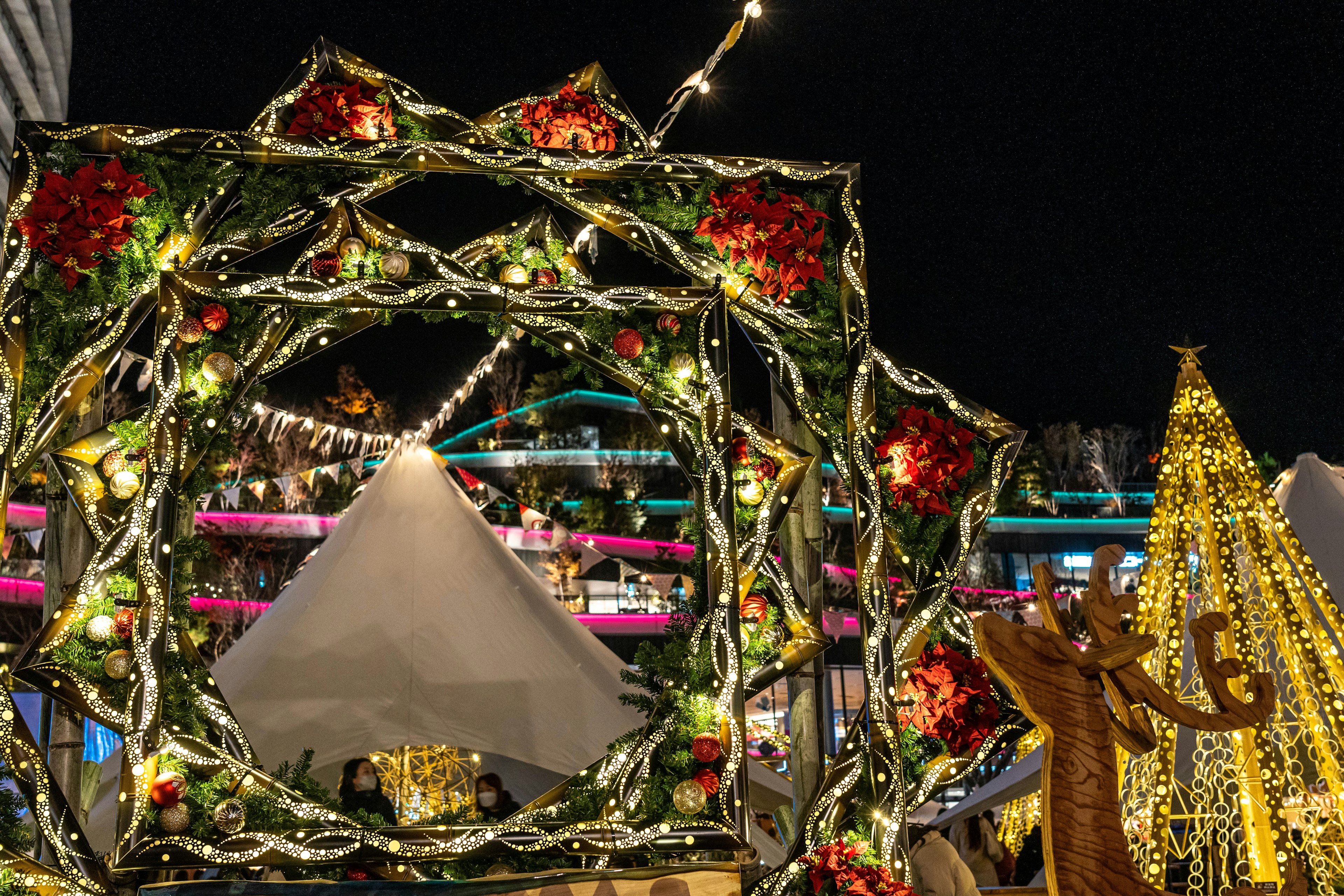 Escena nocturna con decoraciones navideñas que incluyen árboles brillantes y una corona