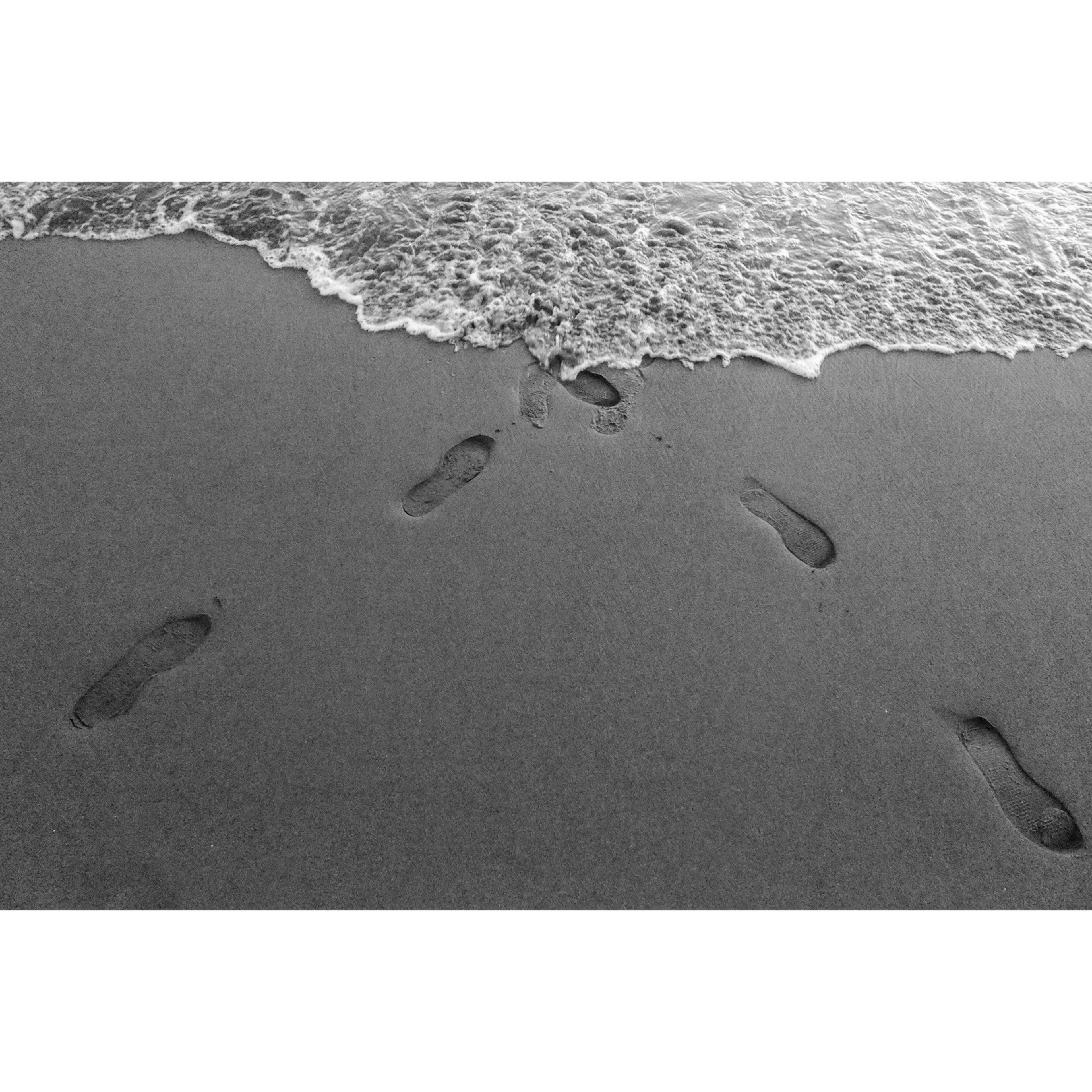 Fussabdrücke am Strand, die auf die Wellen treffen