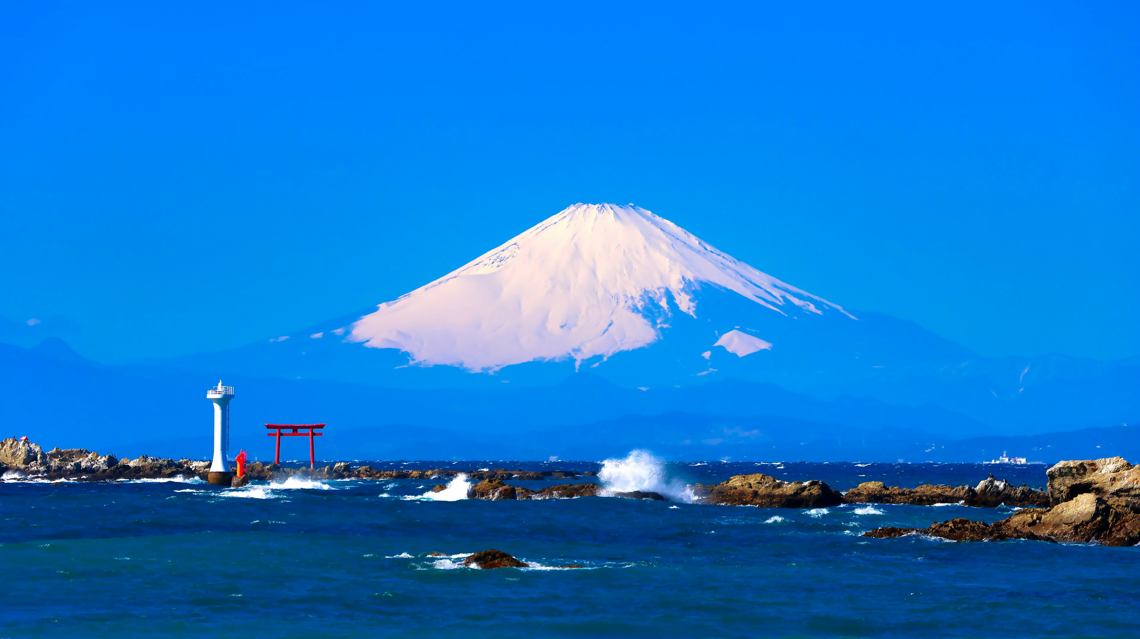 富士山在晴朗的蓝天下巍峨耸立，前景有一个红色的鸟居