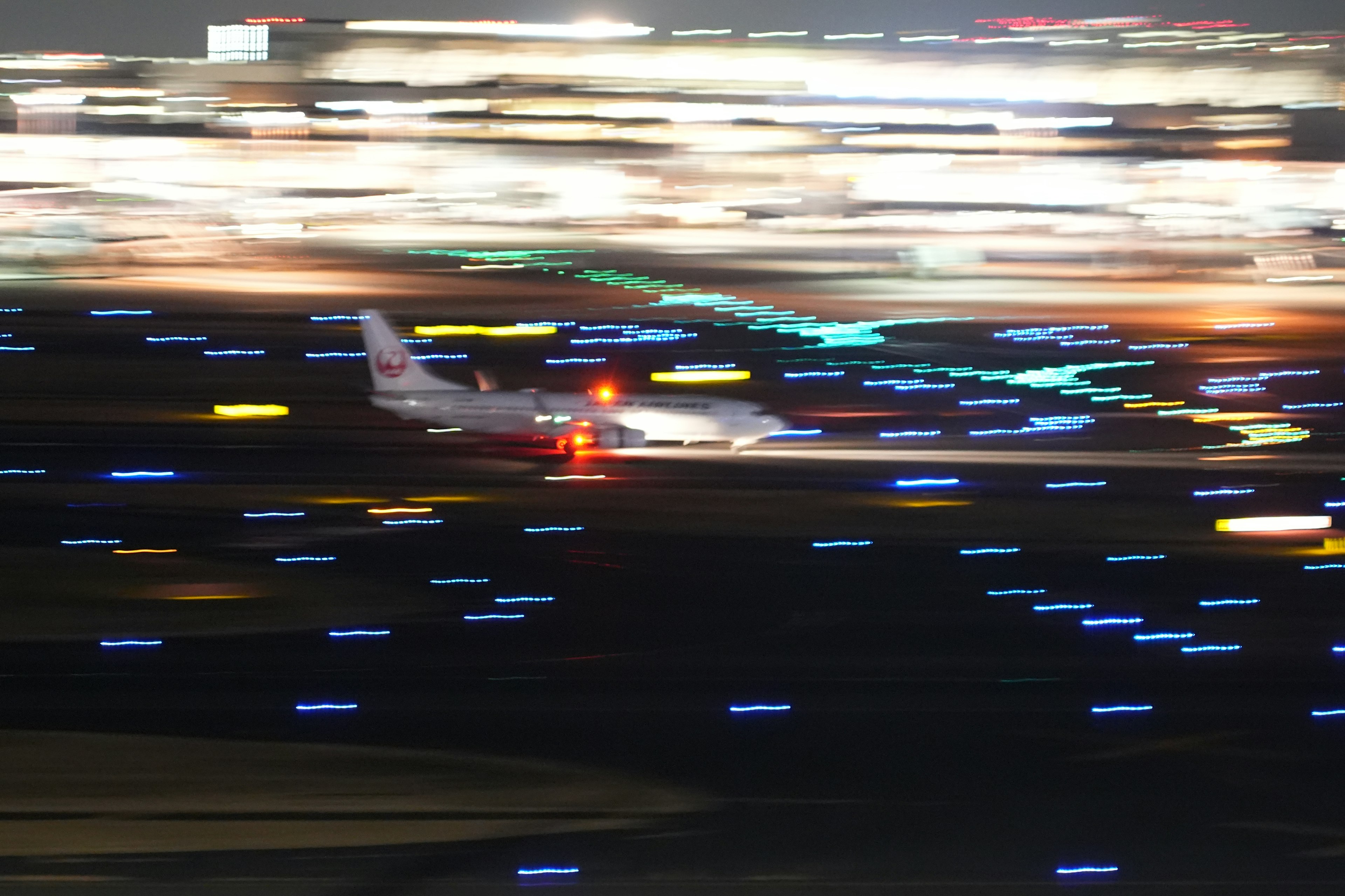 An airplane taxiing on a runway at night with vibrant light spots in the background