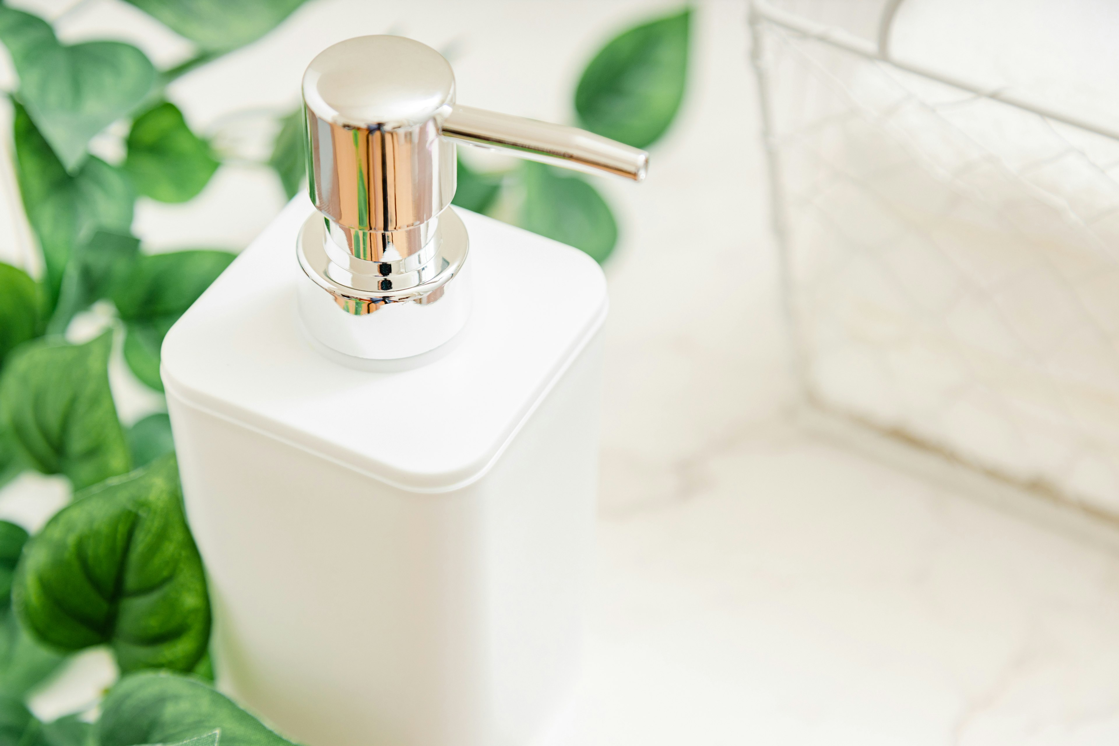 White pump dispenser bottle surrounded by green leaves in a minimalist setting