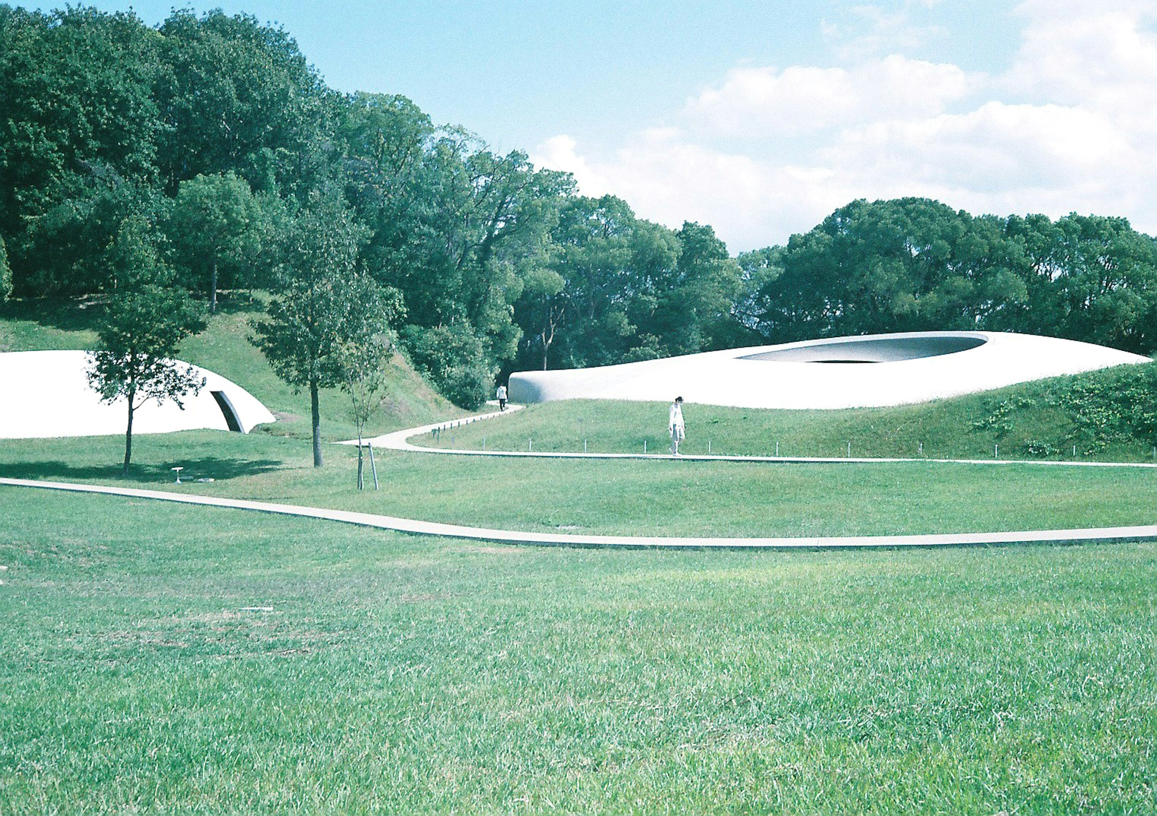 Futuristic white buildings surrounded by green grass and a person