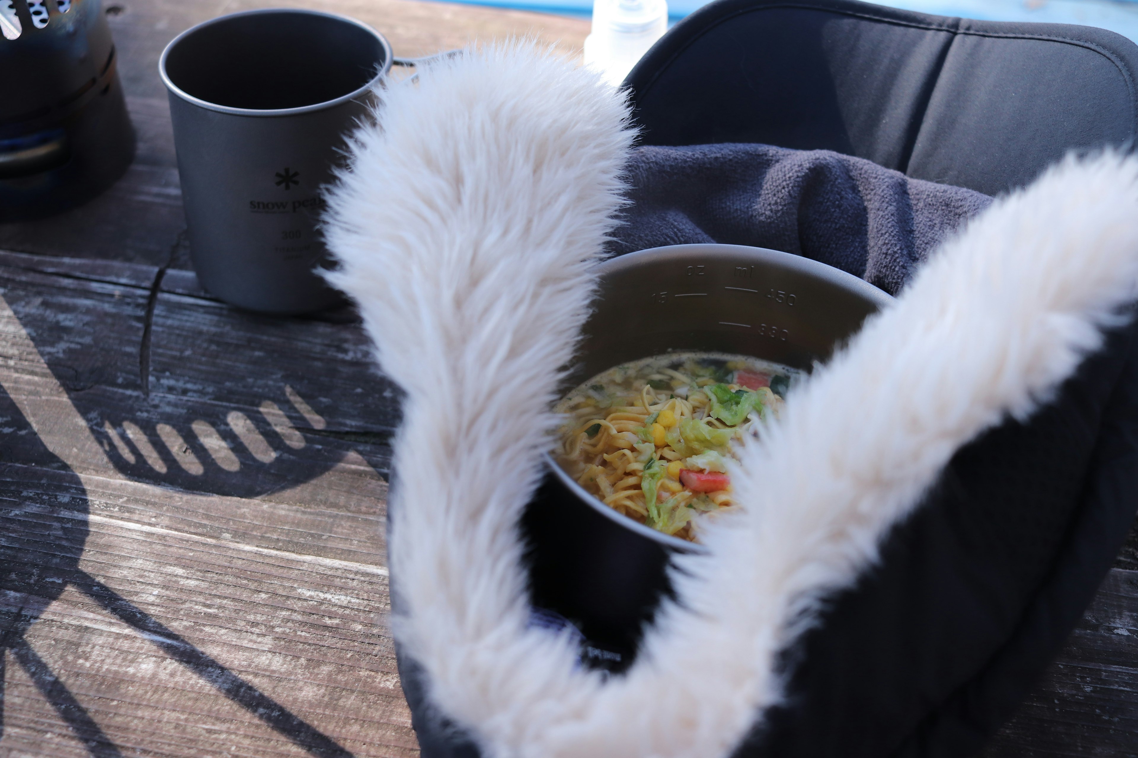 A pot of noodles with colorful vegetables surrounded by a furry handle in a camping scene