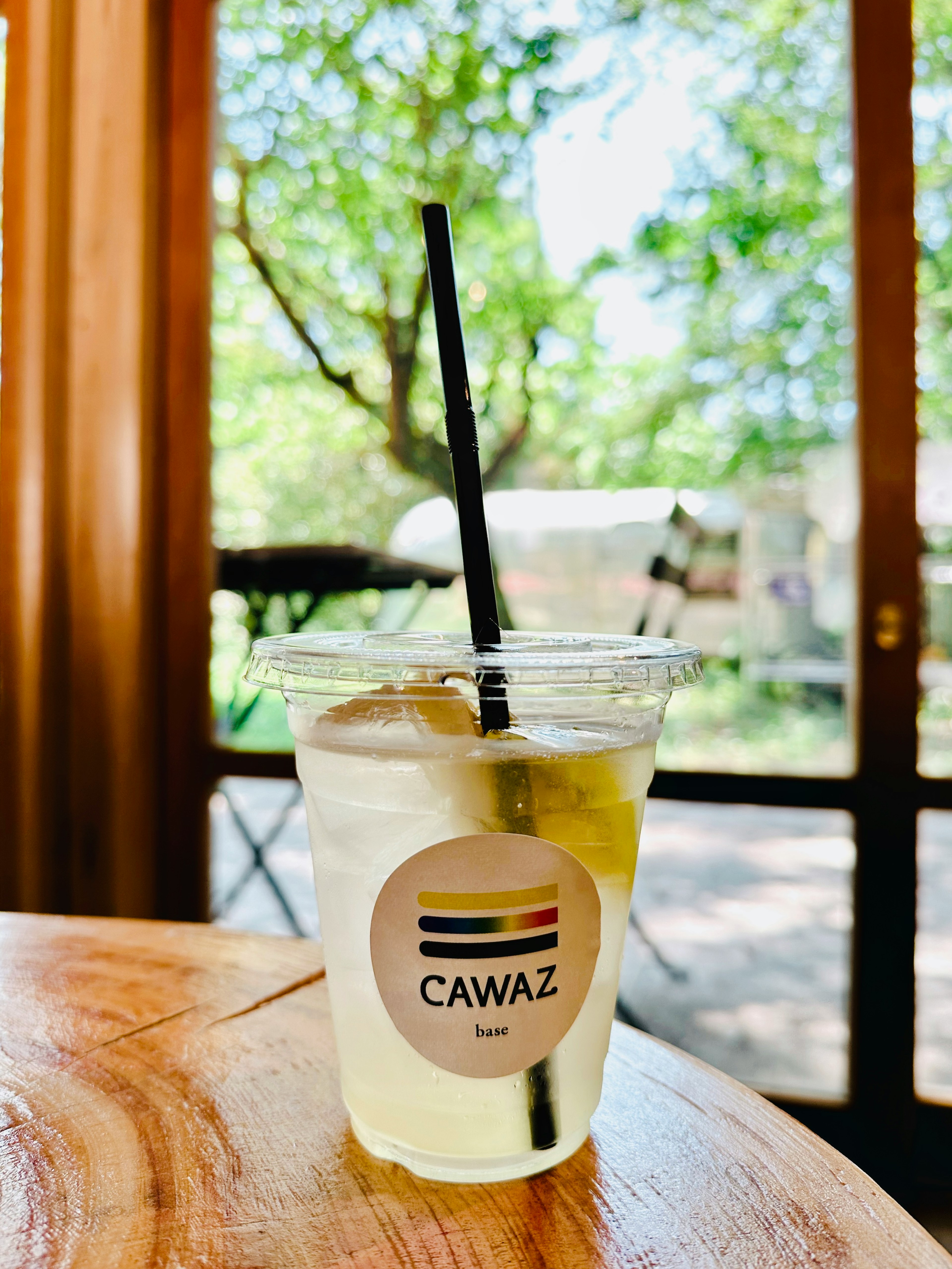 A clear cup with a drink and a straw featuring a CAWAZ logo with green trees in the background