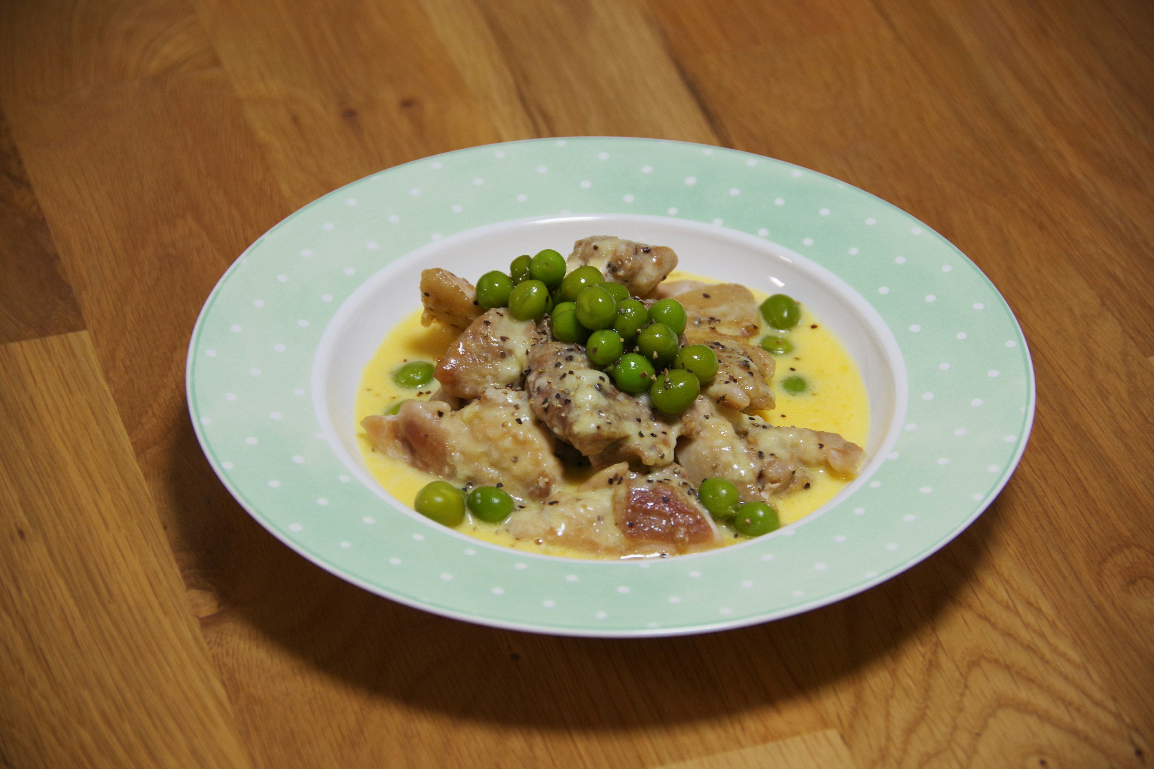 Creamy meat dish topped with green peas served on a decorative plate