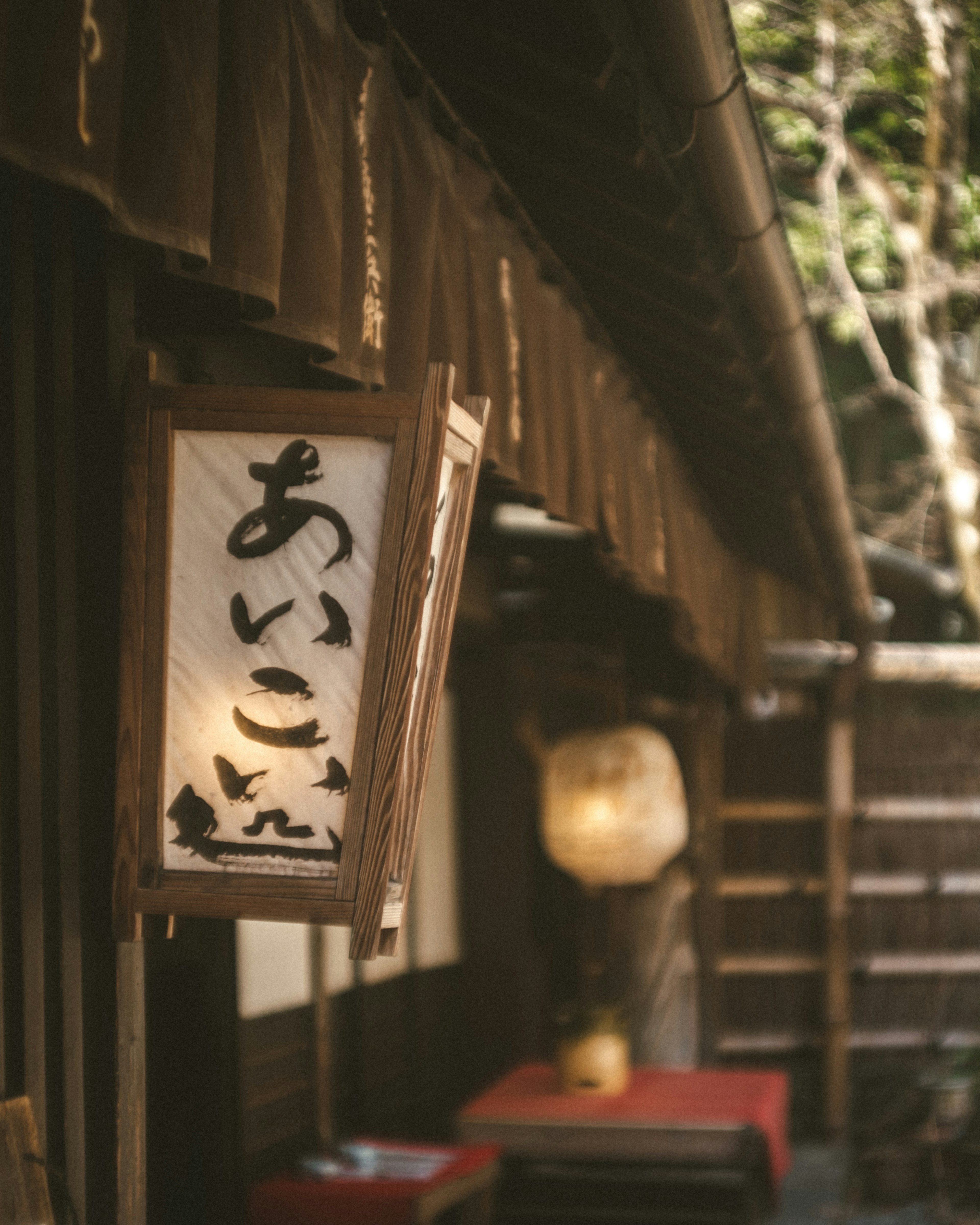 Außenansicht eines traditionellen japanischen Restaurants mit einem Holzschild und einer Laterne vor grünem Hintergrund