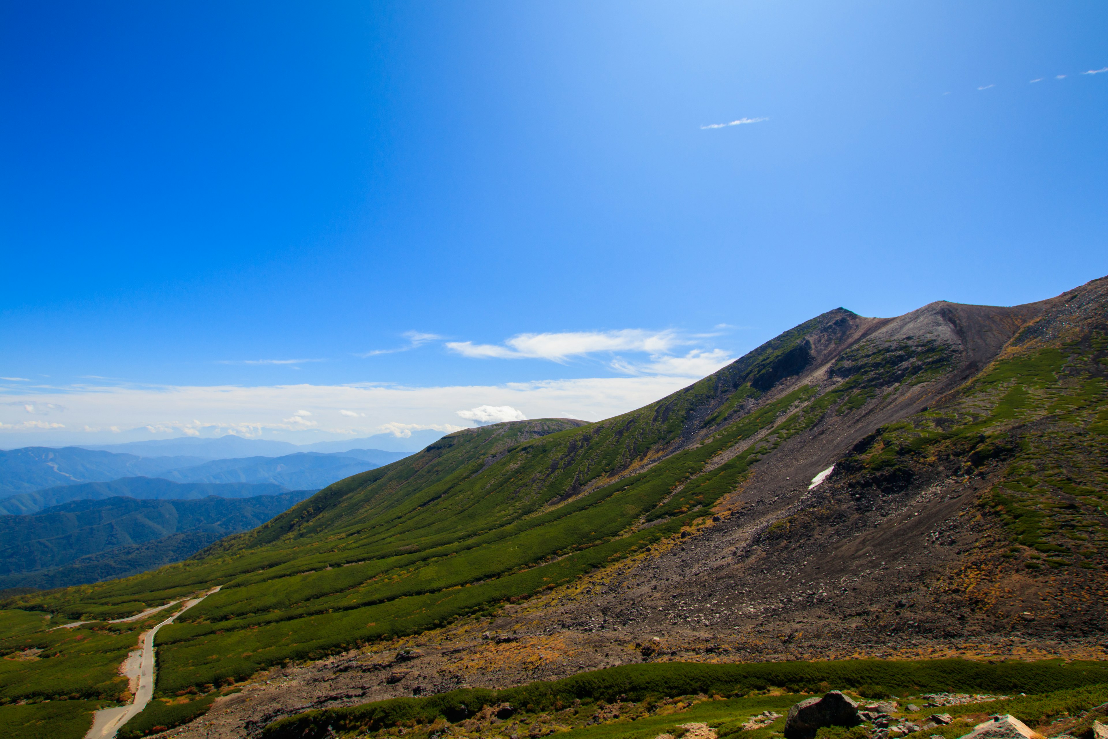 Landschaftsansicht von grünen Hügeln und einem gewundenen Weg unter einem klaren blauen Himmel