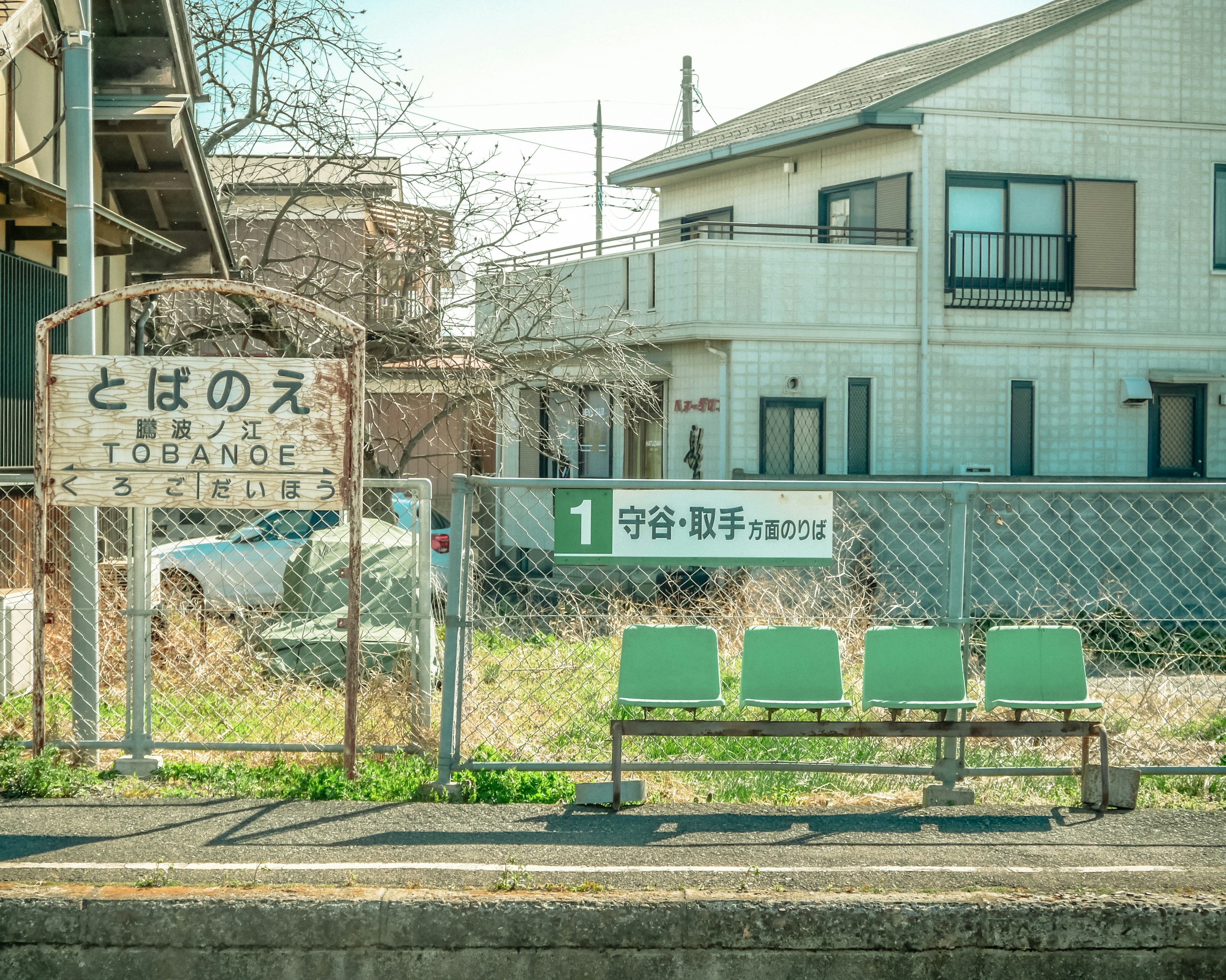 Green benches at a rural train station with an old sign