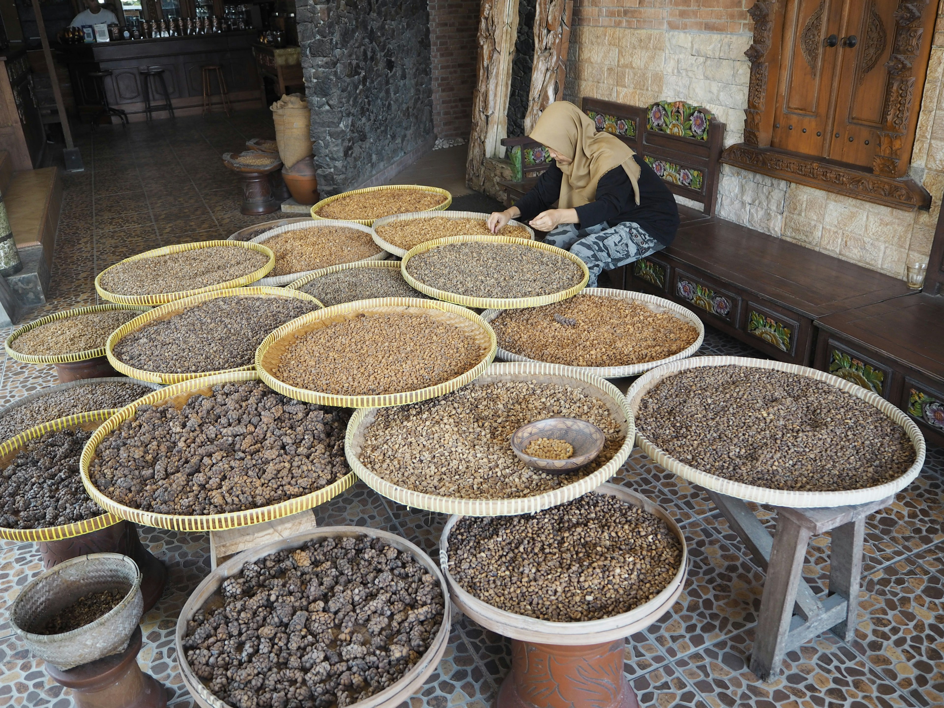 Escena de mercado con varias especias exhibidas en canastas y una mujer trabajando