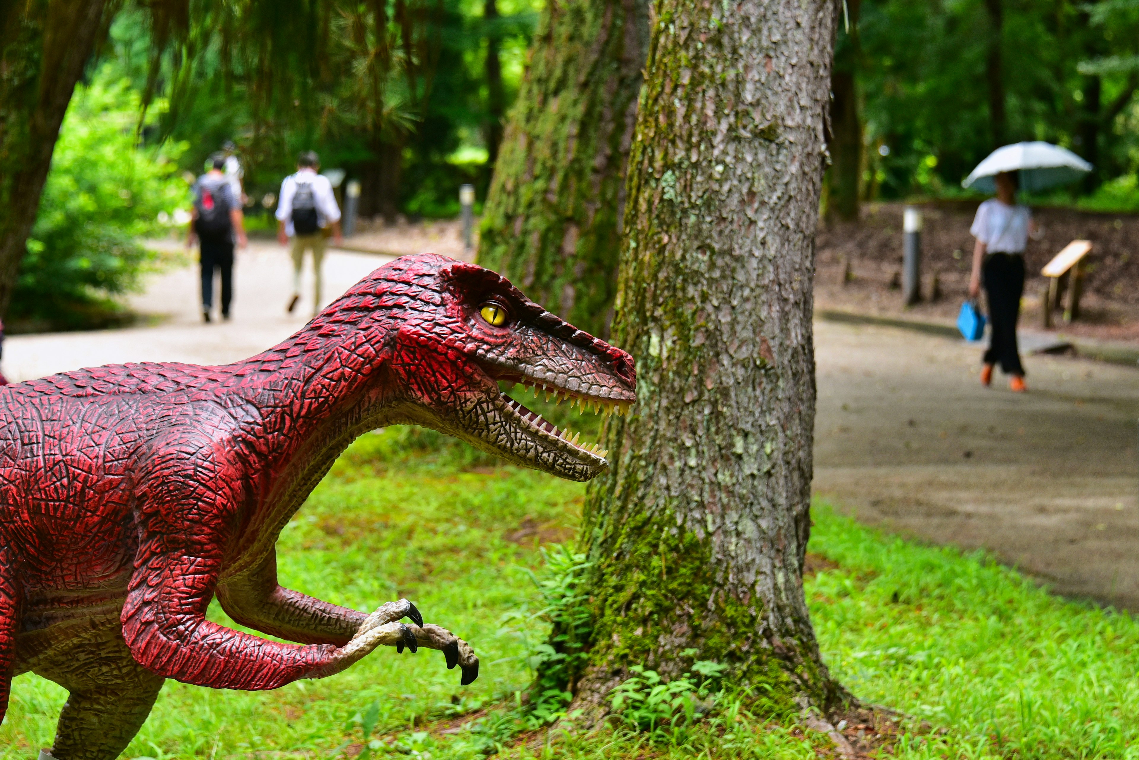 Modelo de dinosaurio en un parque con personas caminando