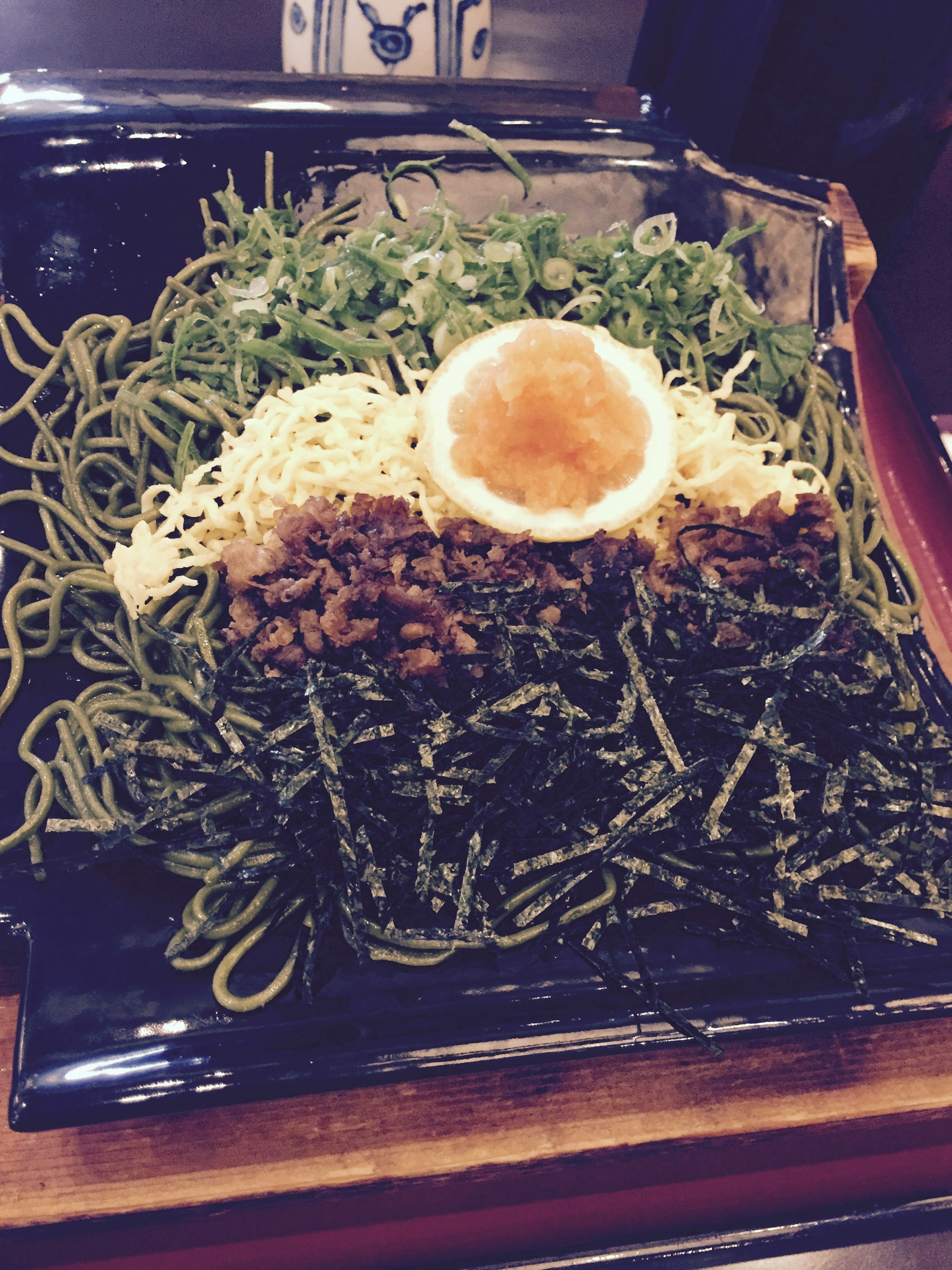 Un plato japonés colorido con fideos verdes cubiertos con huevo, carne y algas