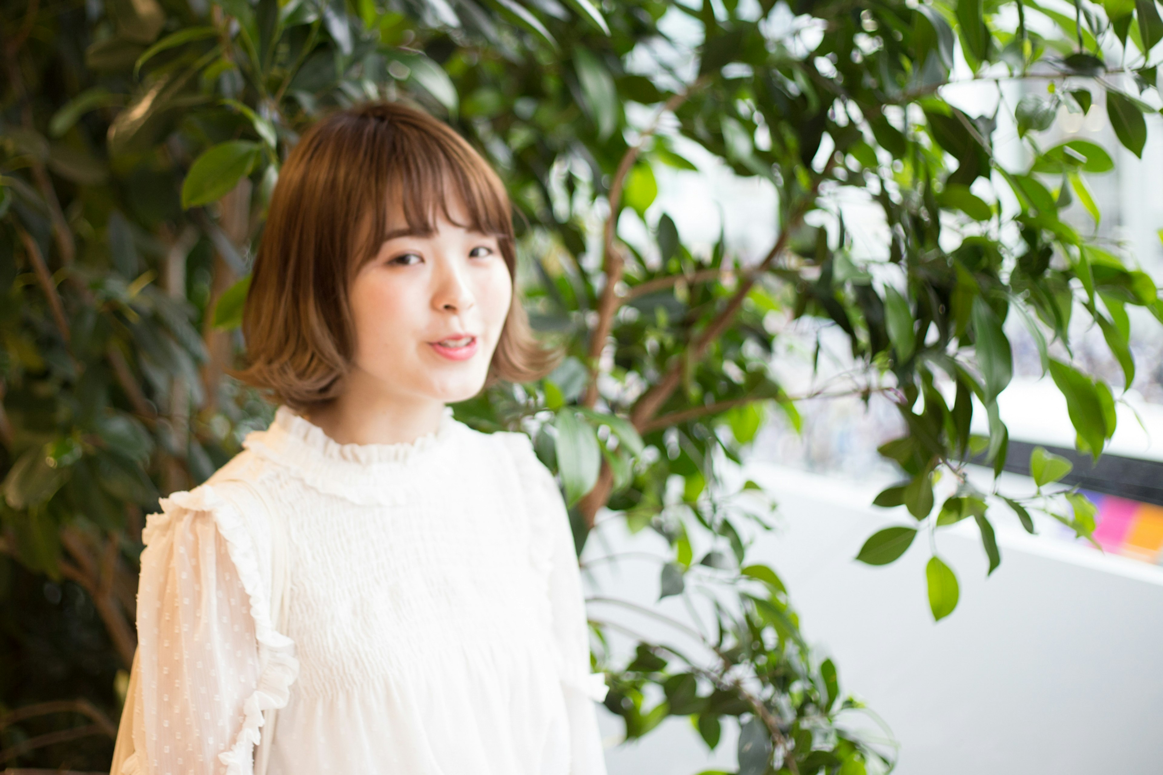 Una mujer con blusa blanca de pie frente a plantas