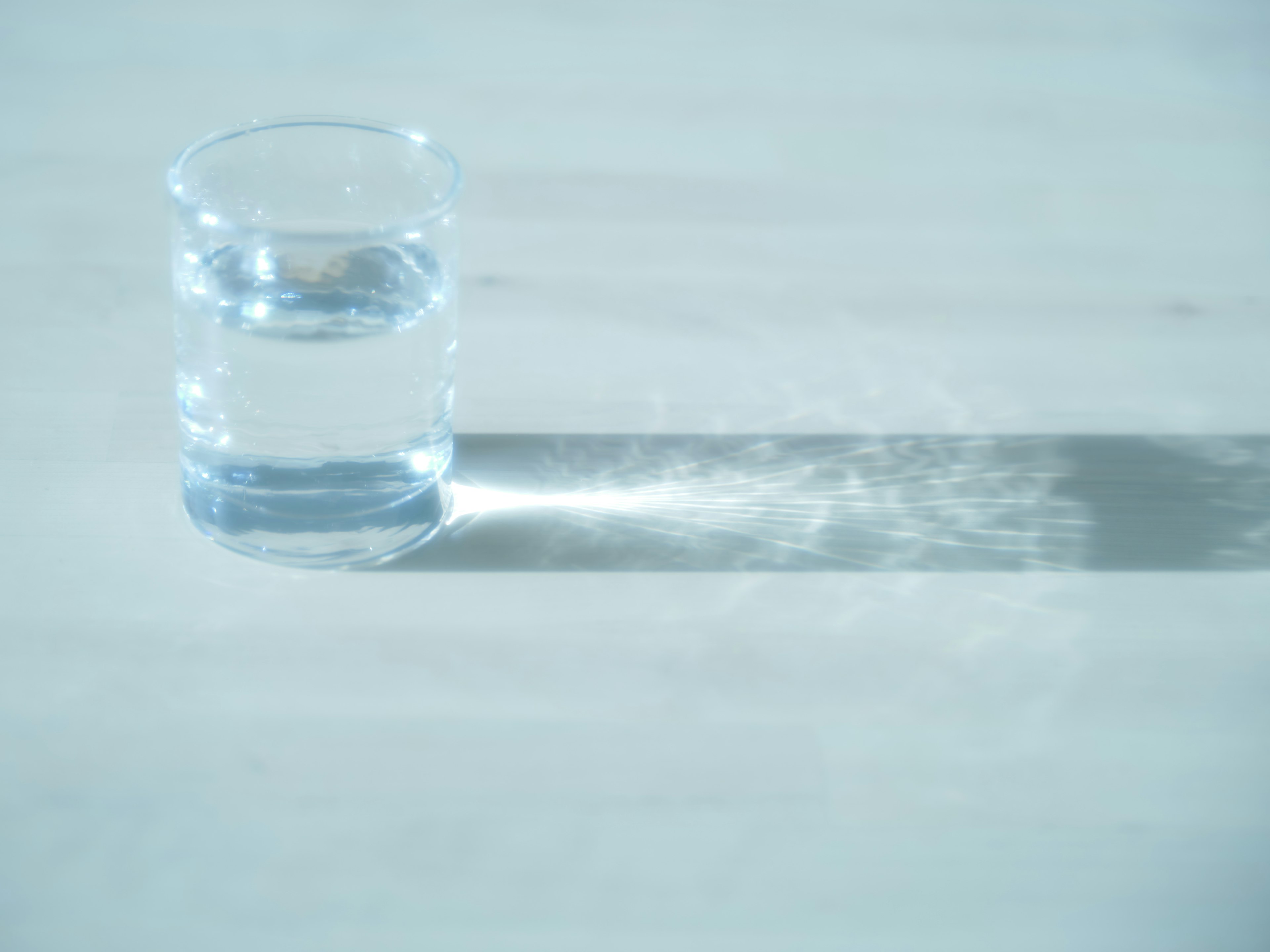 A clear glass of water on a table casting a long shadow