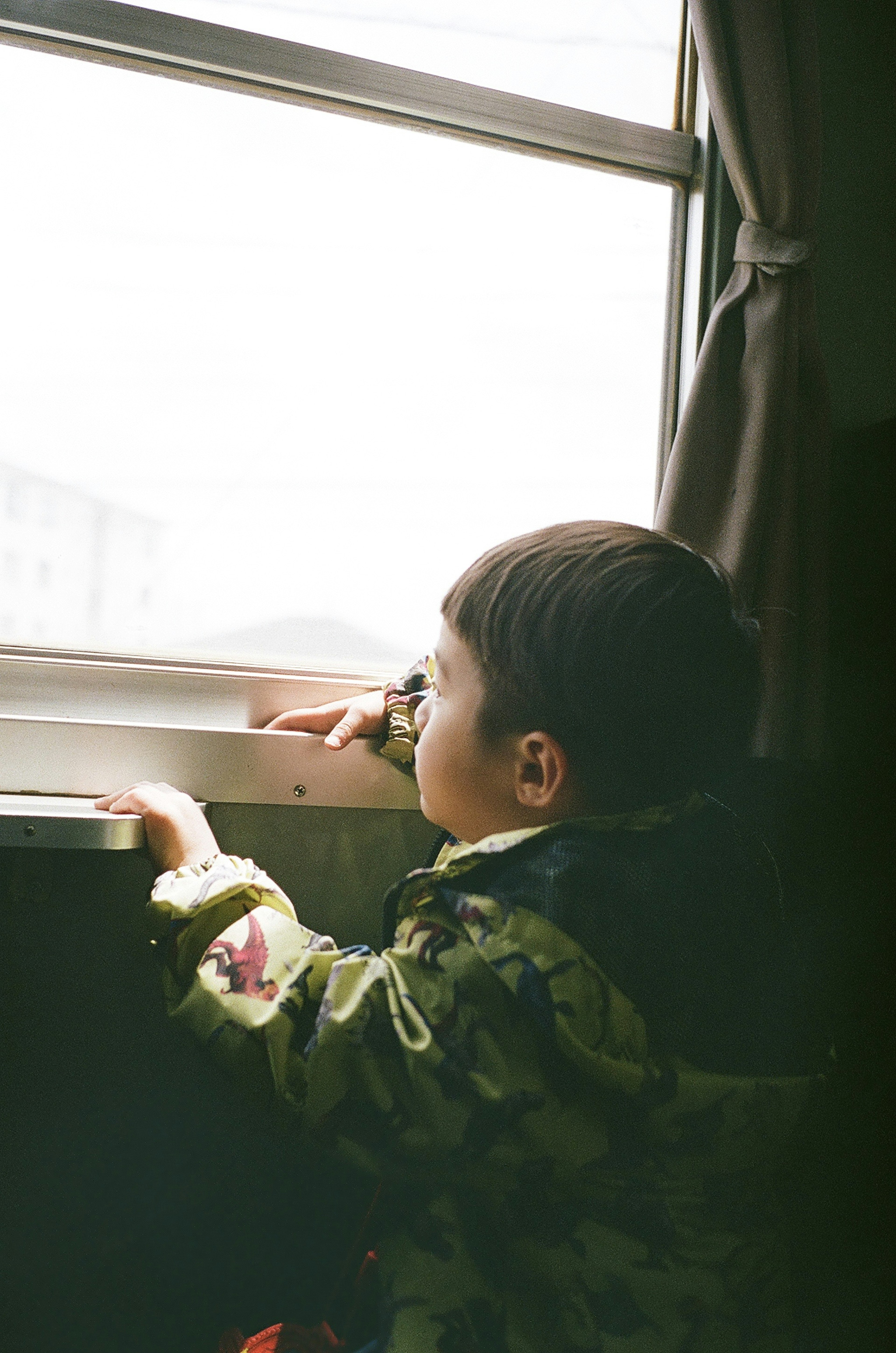 Child looking out the window with a camouflage jacket