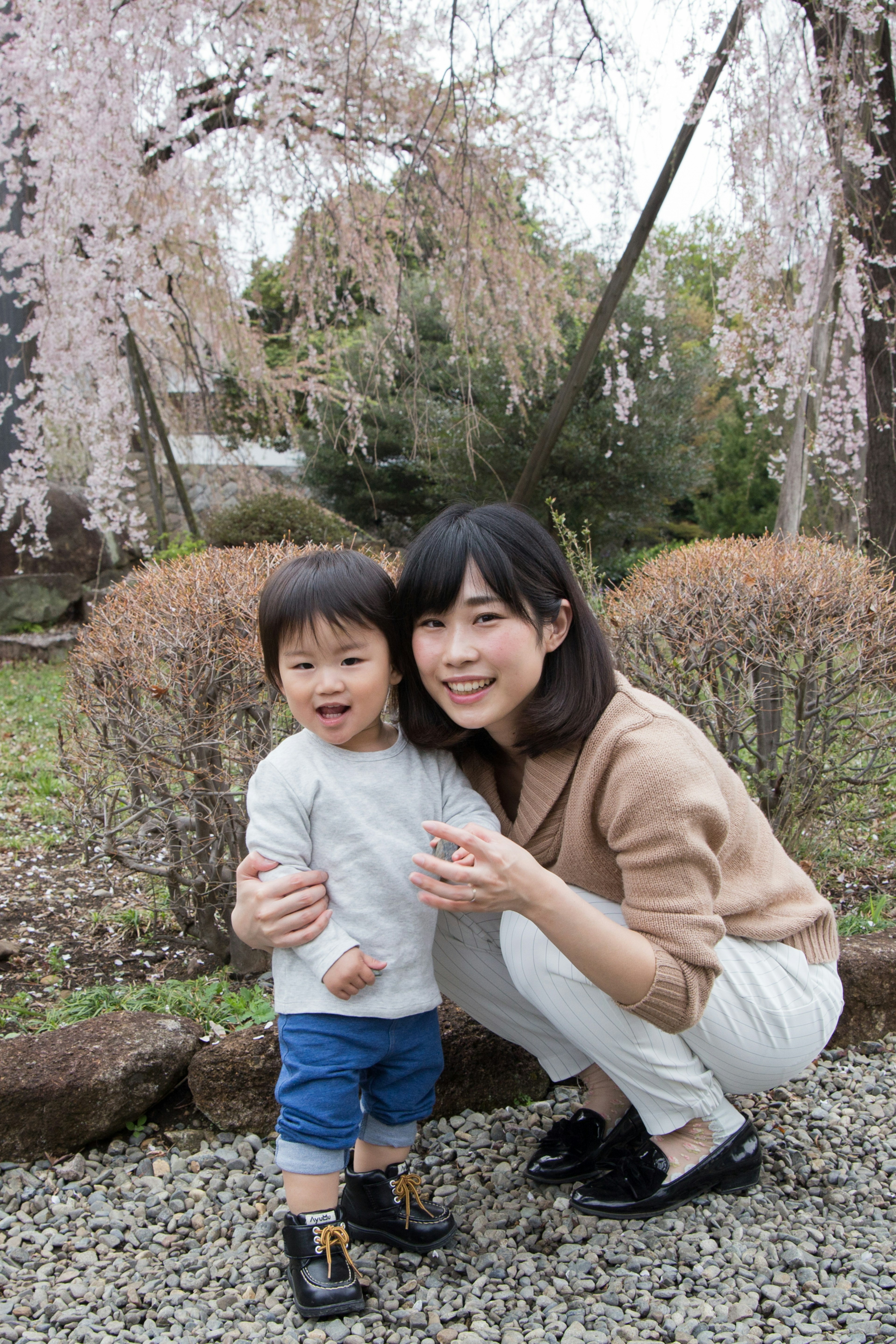 A mother and child smiling in front of cherry blossom trees in a park