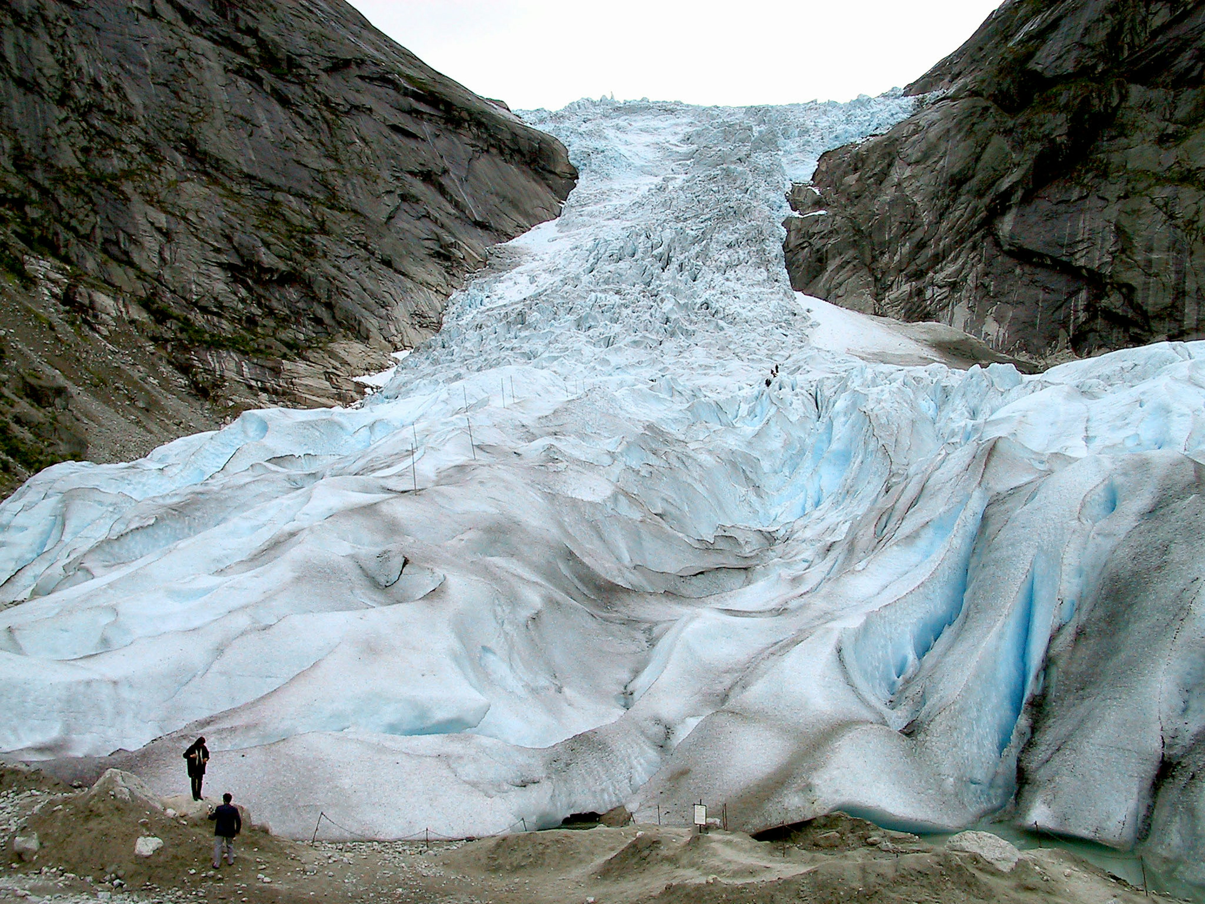 A person standing near a glacier flowing between rocky cliffs