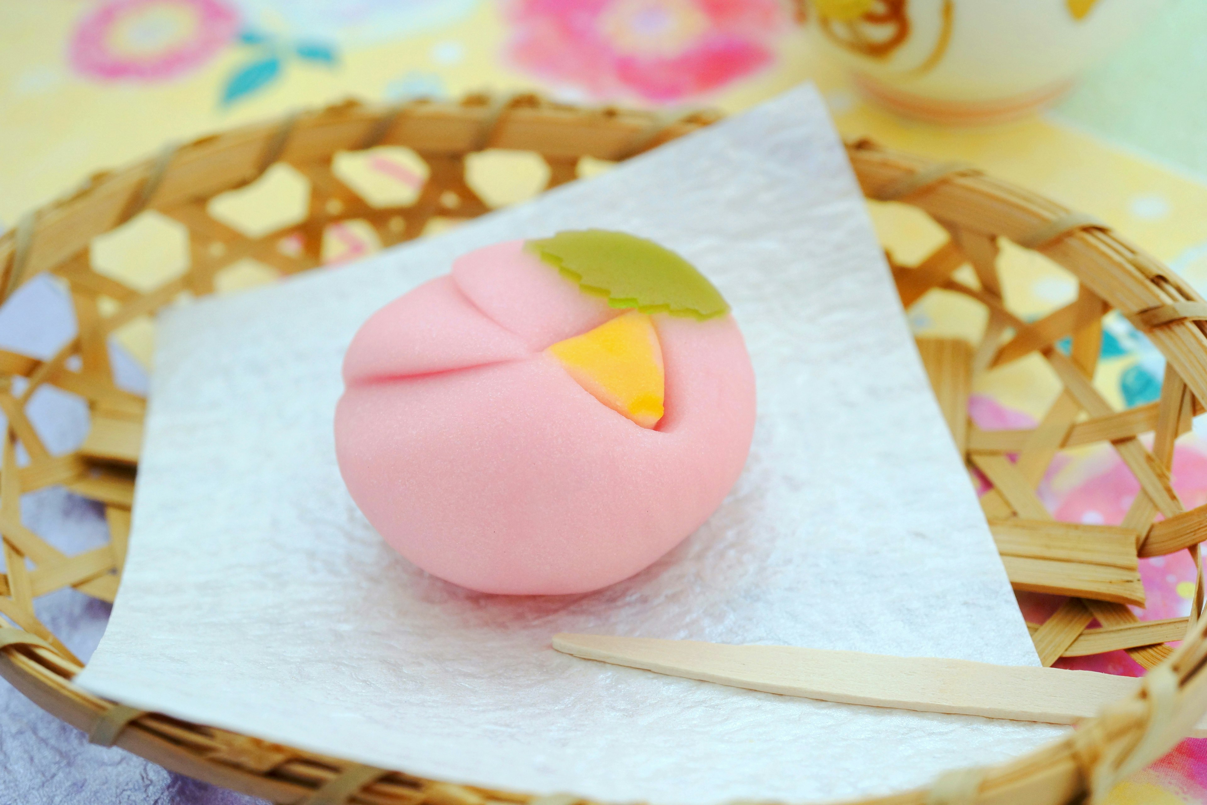 Un wagashi en forme de pêche placé dans un panier en bambou