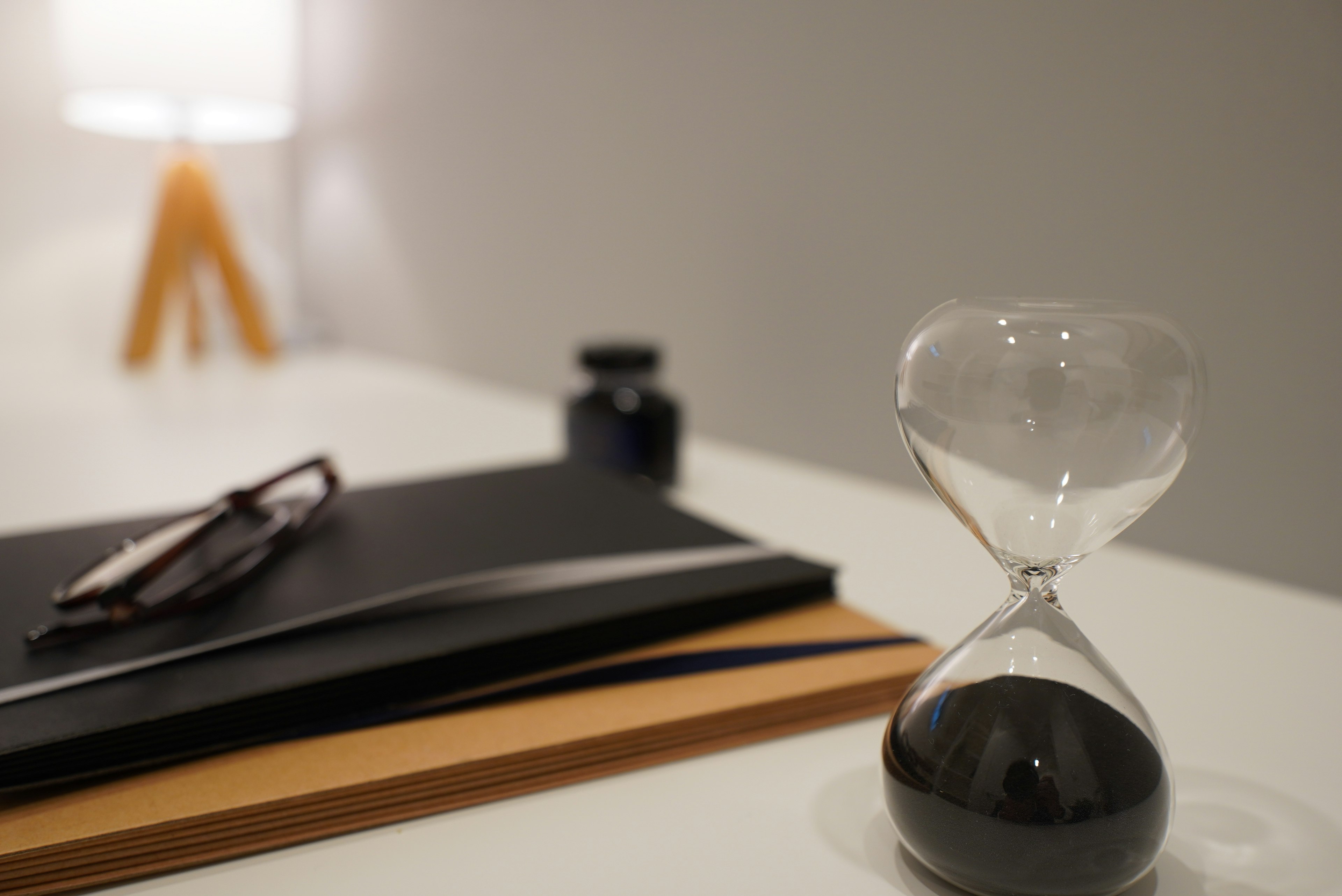 Une scène de bureau avec un sablier à sable noir un carnet noir et un stylo près de lunettes et d'une bouteille d'encre