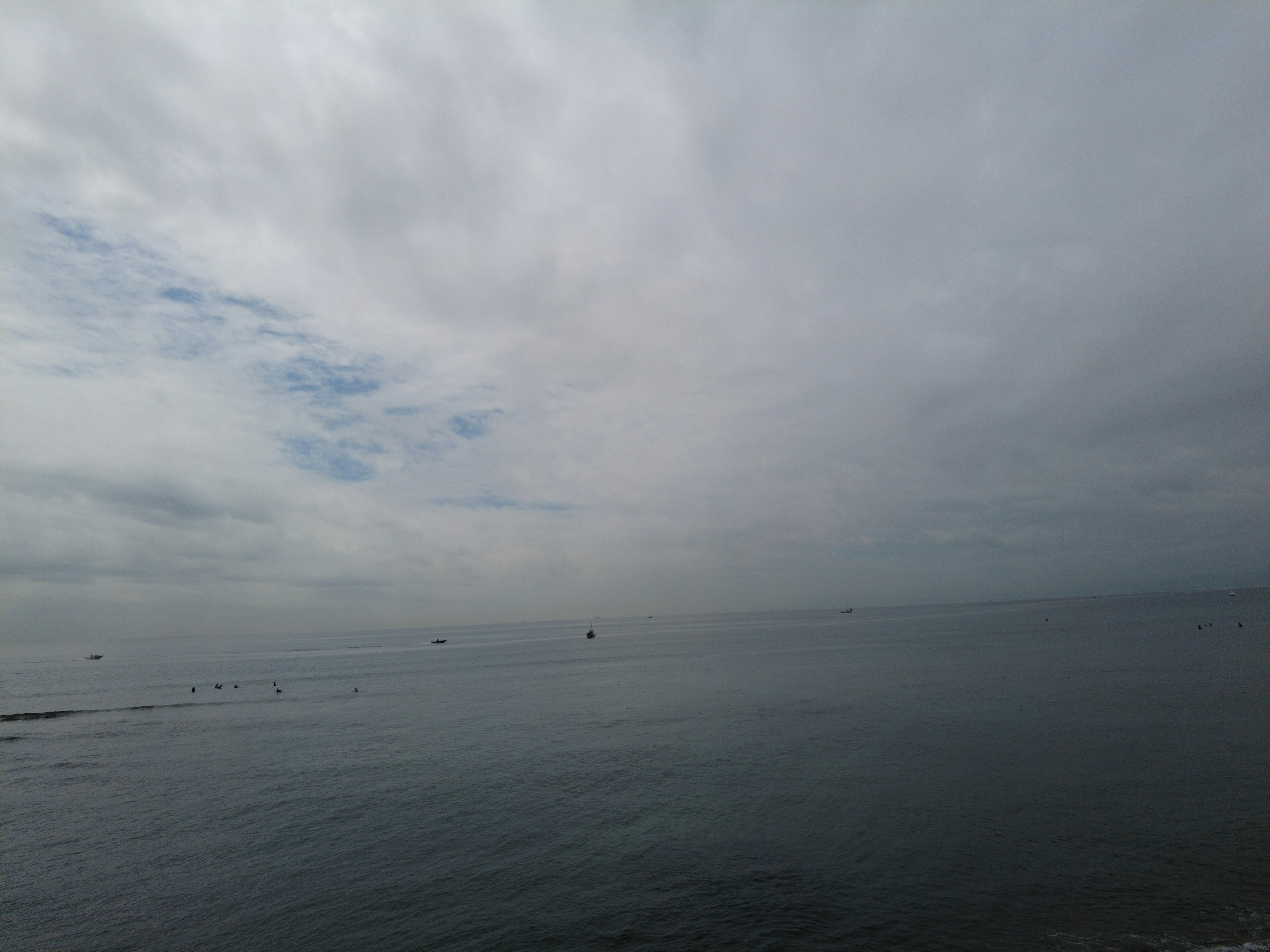 Calm sea landscape under a cloudy sky with small boats in the distance