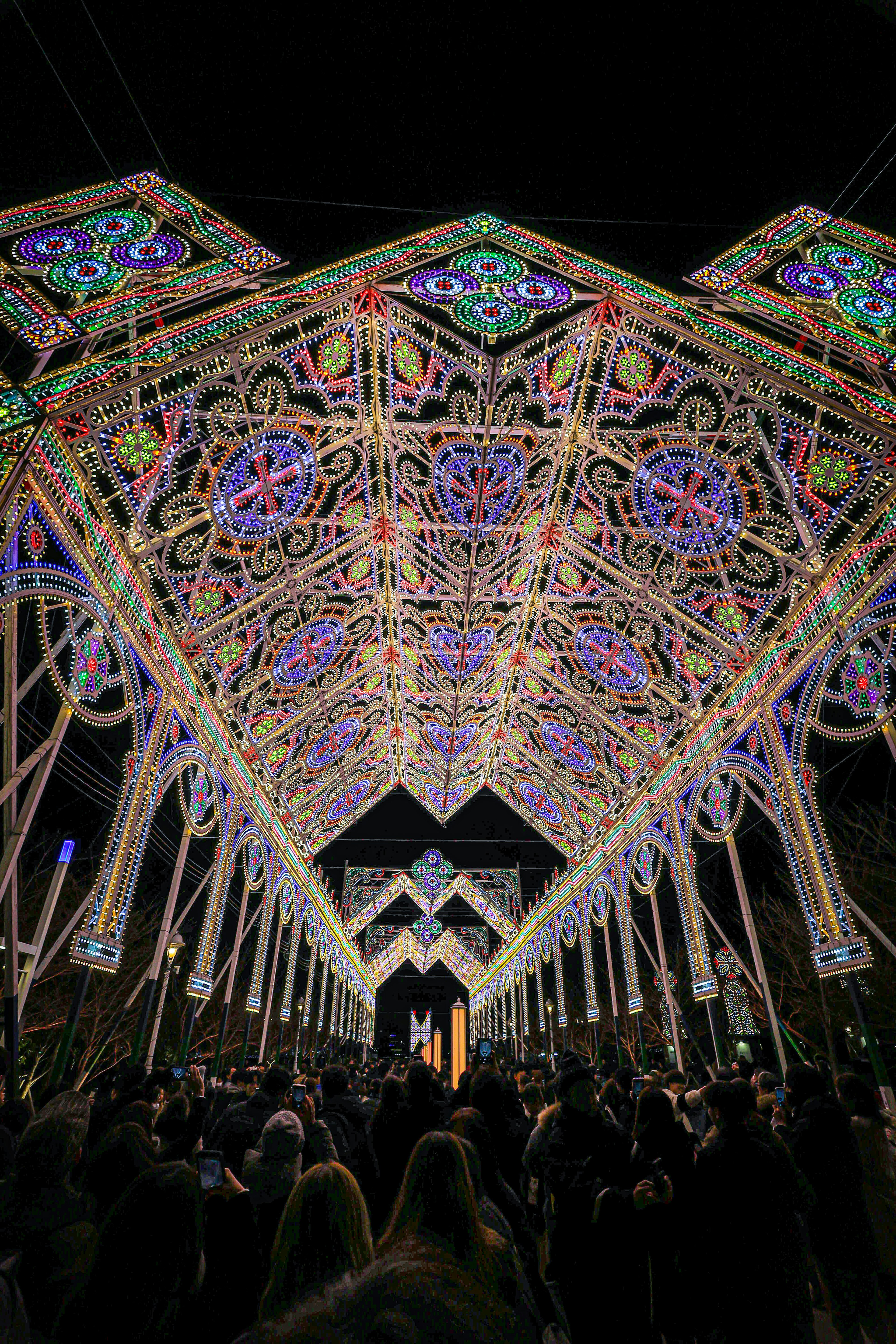 Bellissima struttura ad arco illuminata di notte con luci colorate e folle di visitatori