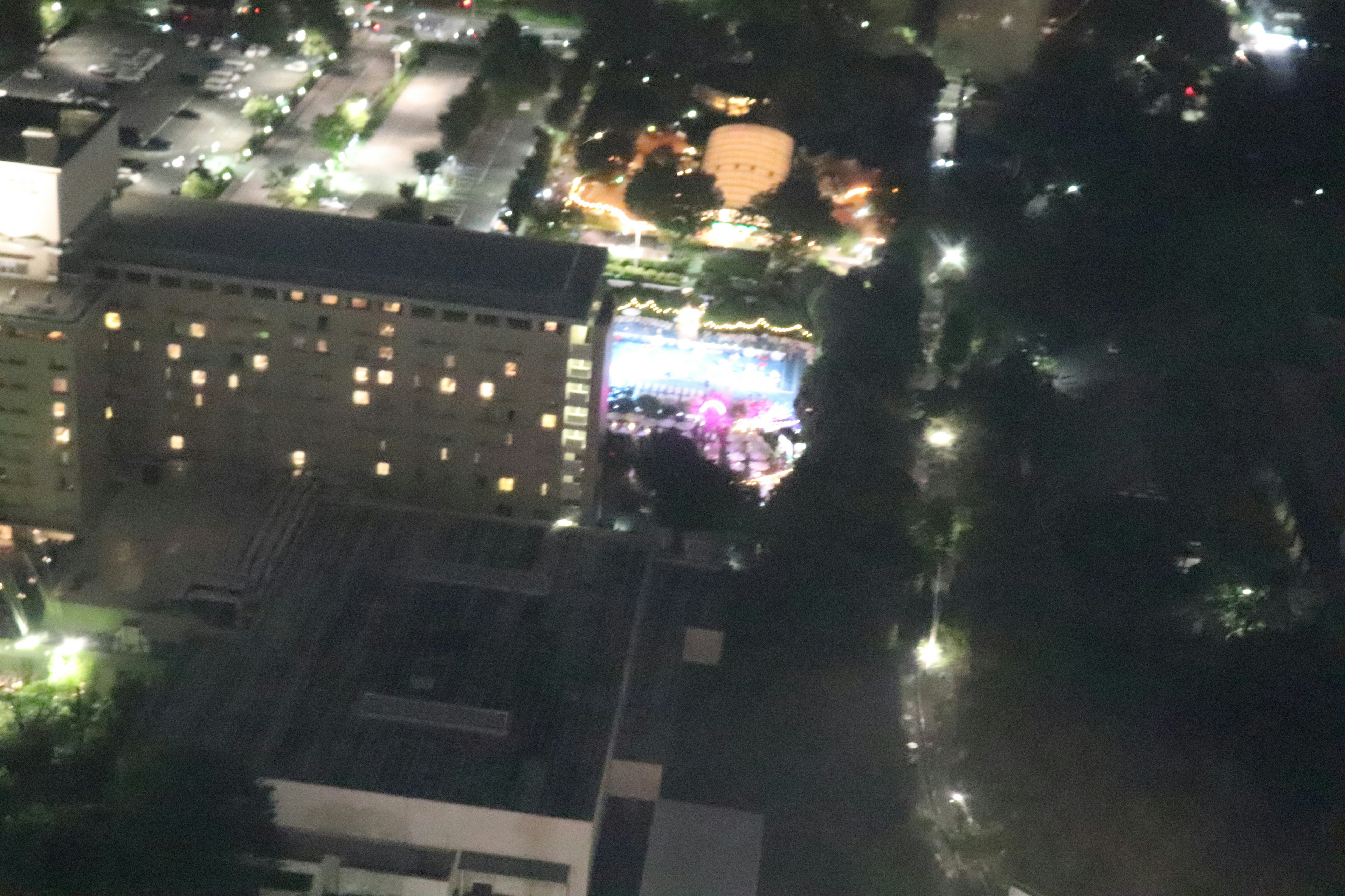 Aerial view of a colorful event space illuminated at night surrounded by buildings and trees