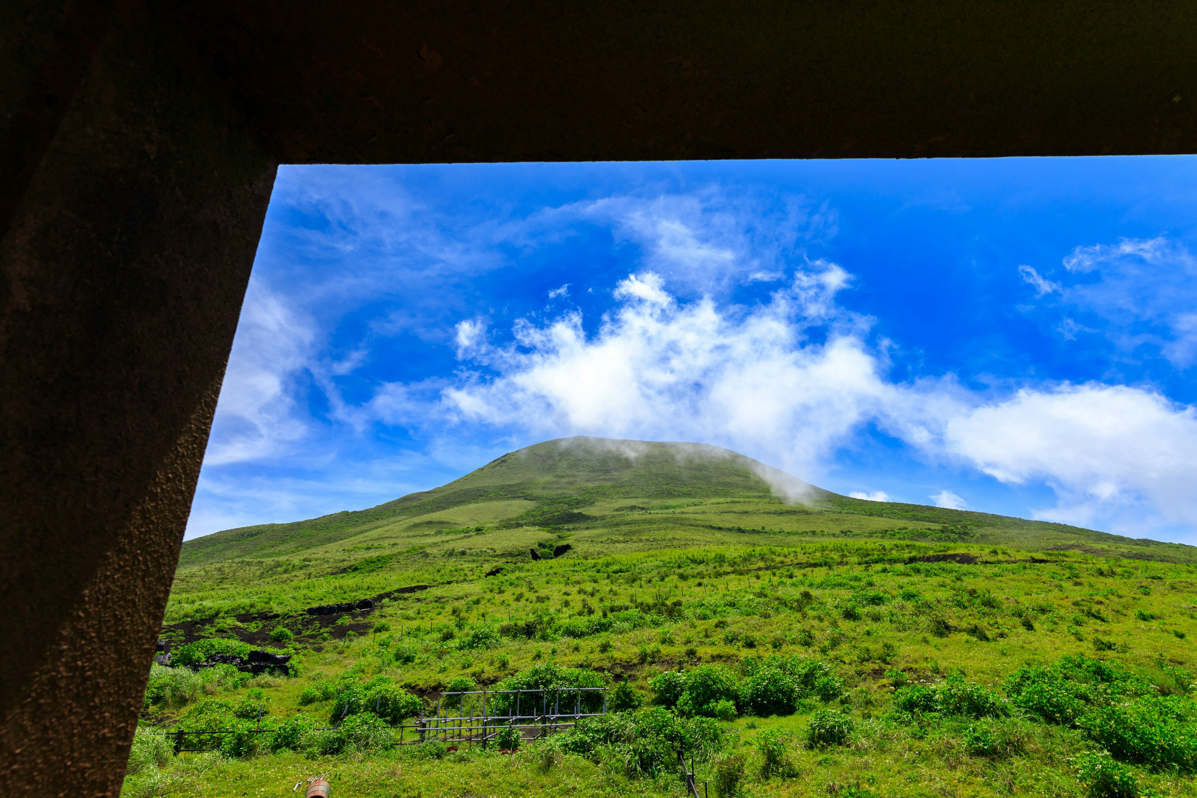 Lush green mountain landscape under a blue sky with clouds