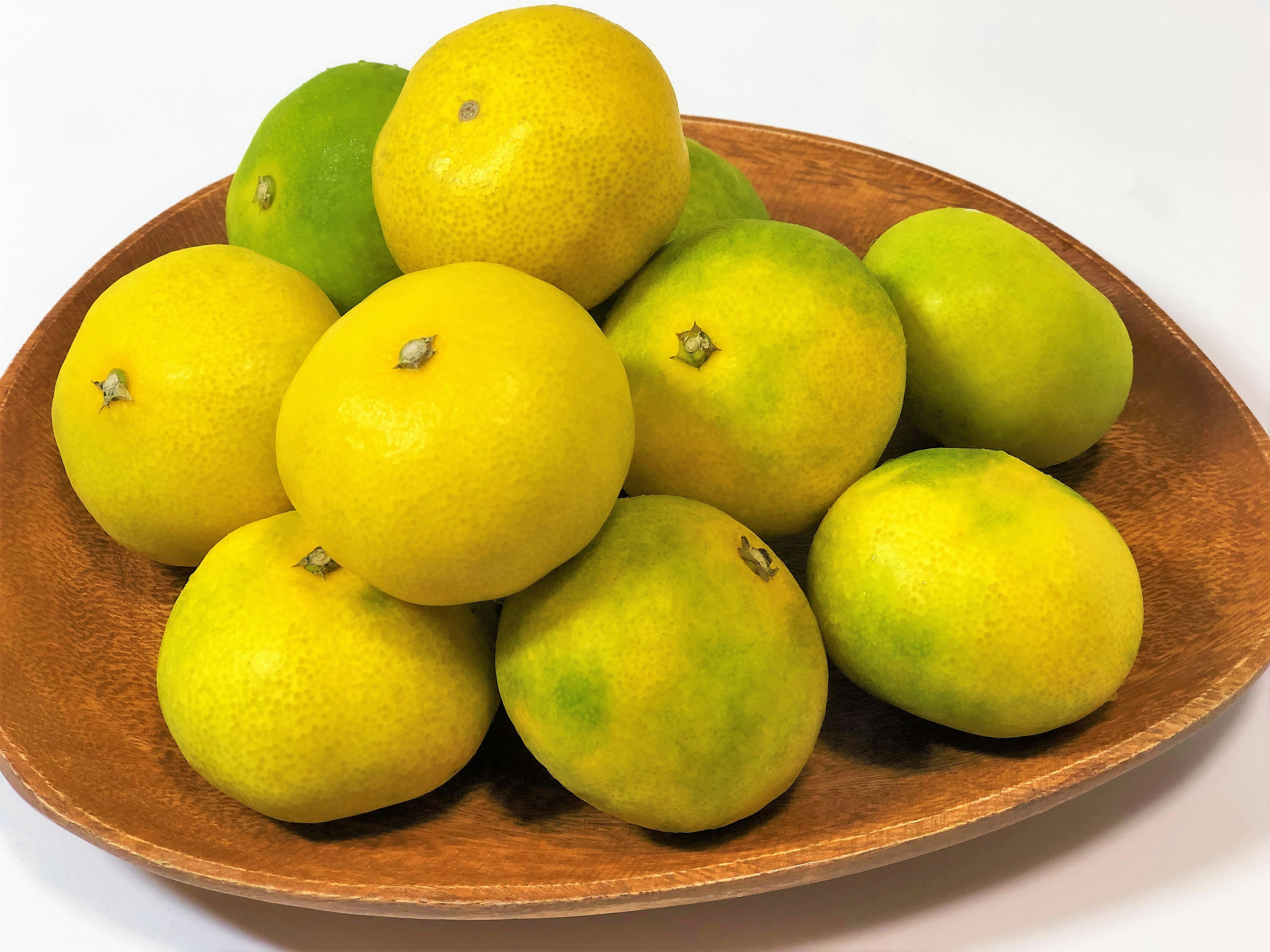 A pile of yellow and green citrus fruits on a wooden plate