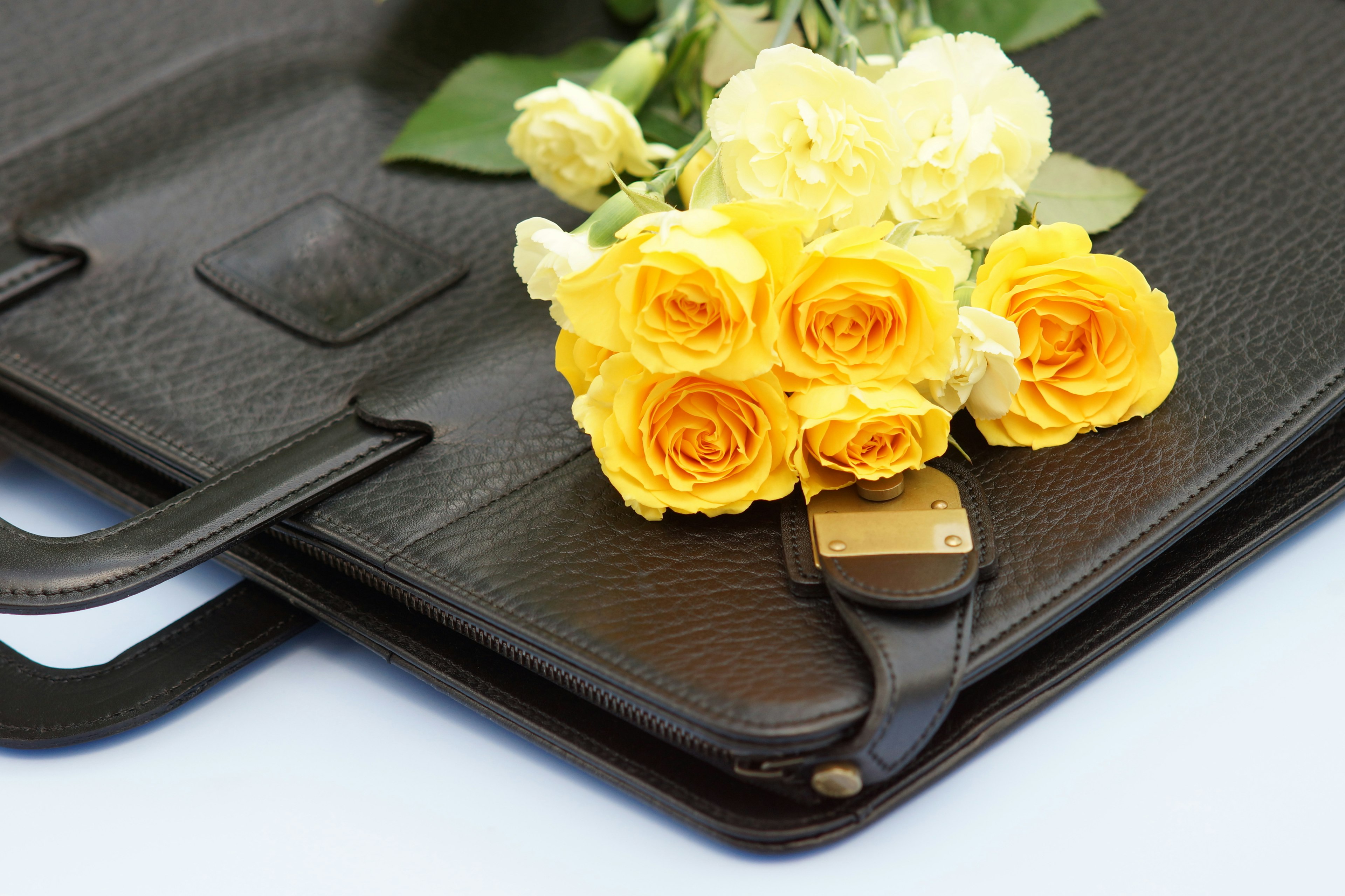 Ein Strauß aus gelben Rosen und weißen Blumen auf einer schwarzen Ledertasche