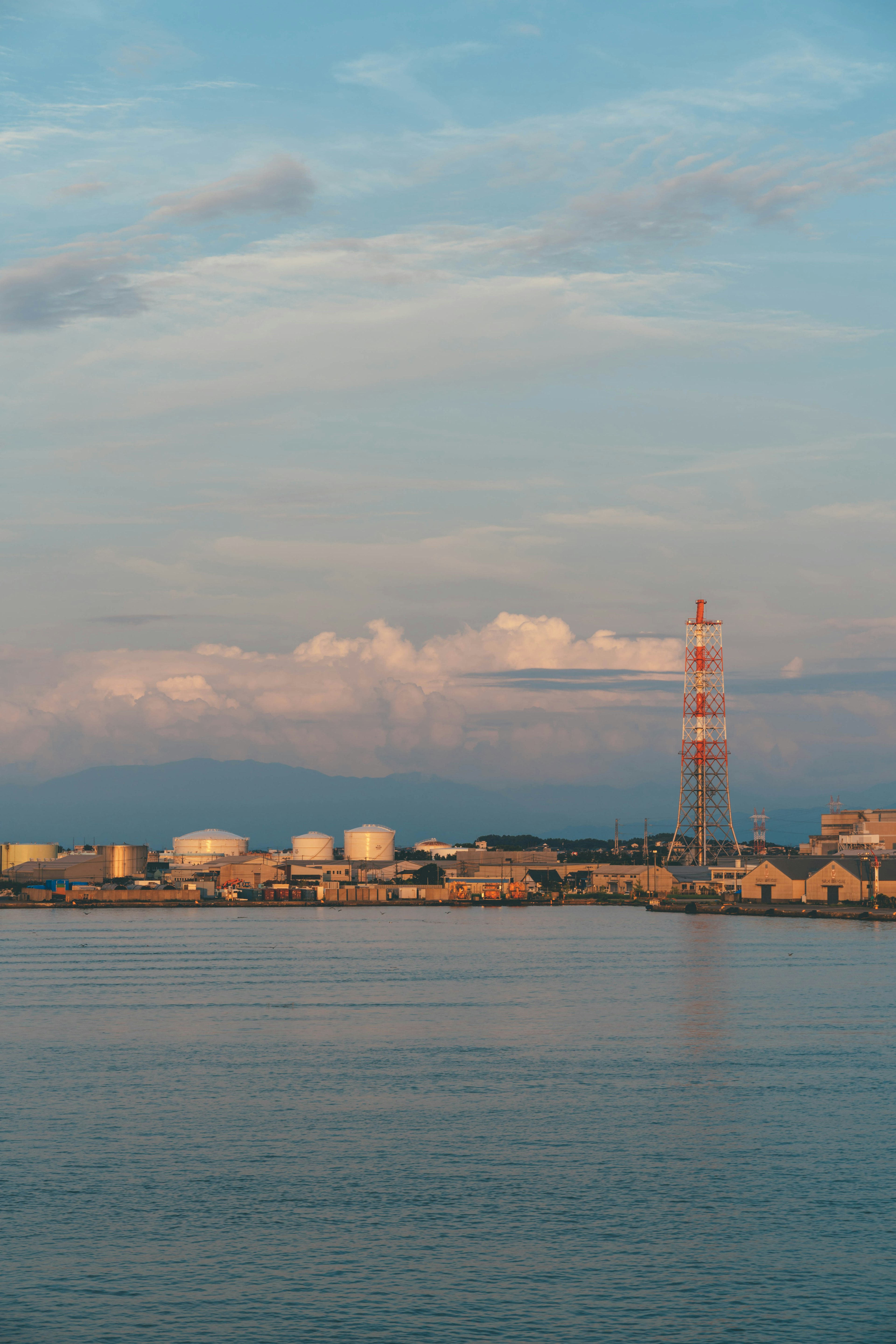 Paesaggio industriale con torre di comunicazione e serbatoi di stoccaggio su sfondo di mare e cielo blu