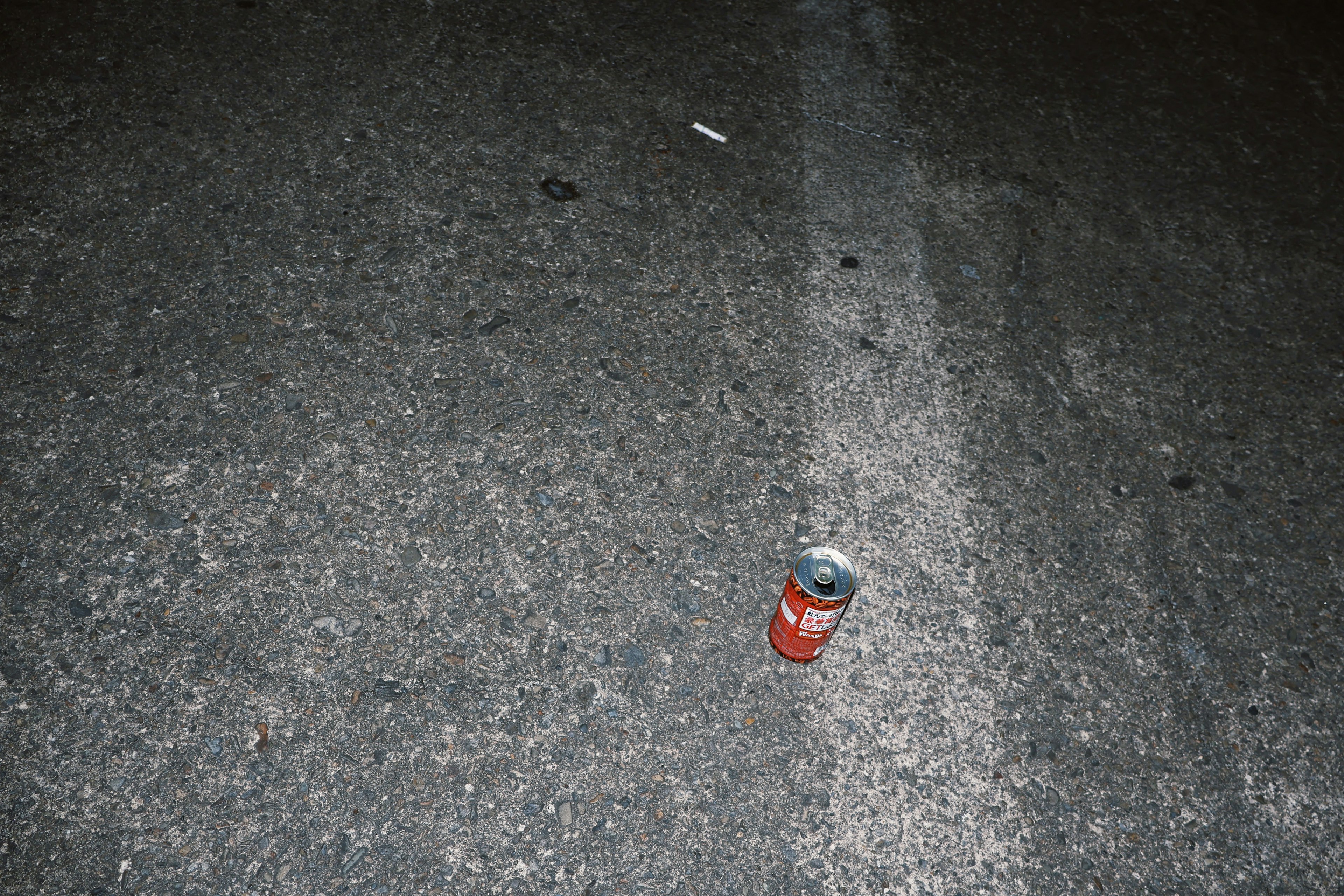 Une canette rouge posée sur une surface de route sombre