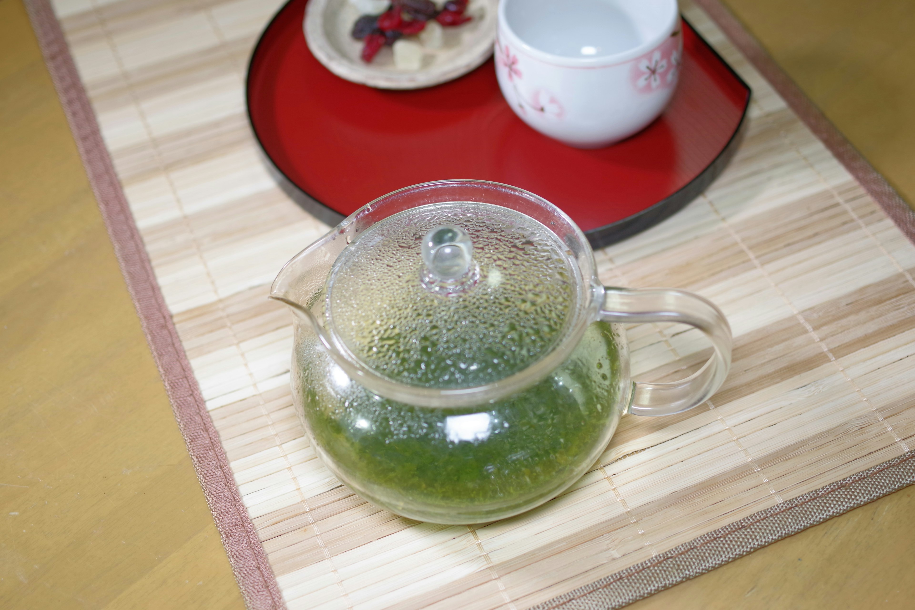 Théière en verre avec du thé vert et une tasse sur un tapis en bois