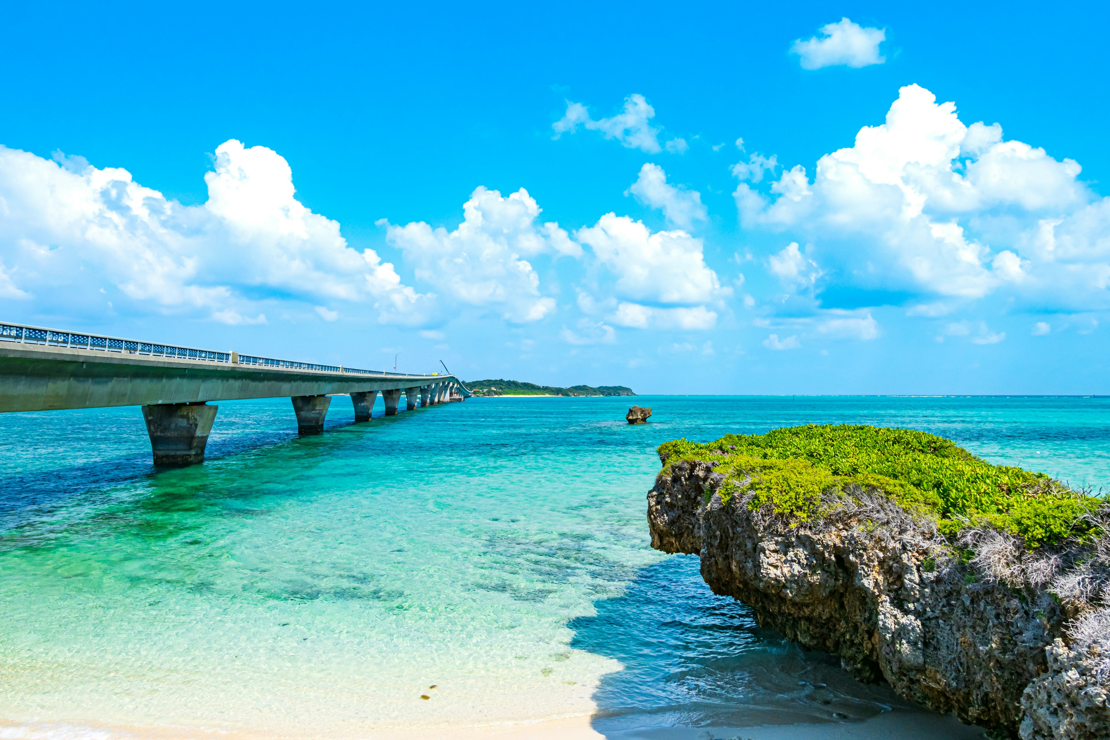 Scenic view of a vibrant blue sky with fluffy clouds over a clear turquoise sea and a bridge