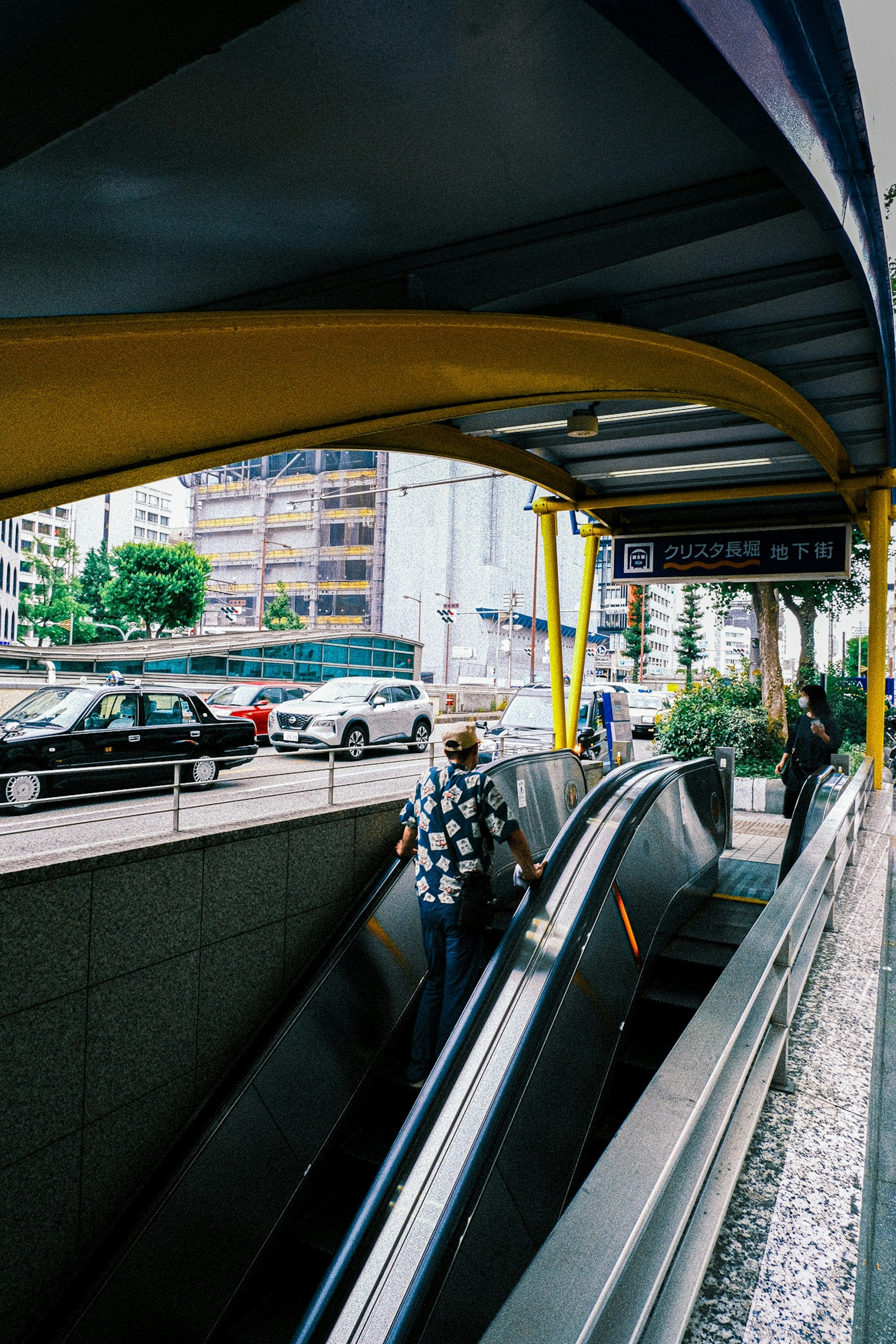 Entrée d'un escalier mécanique avec un arc jaune distinctif et un paysage urbain en arrière-plan