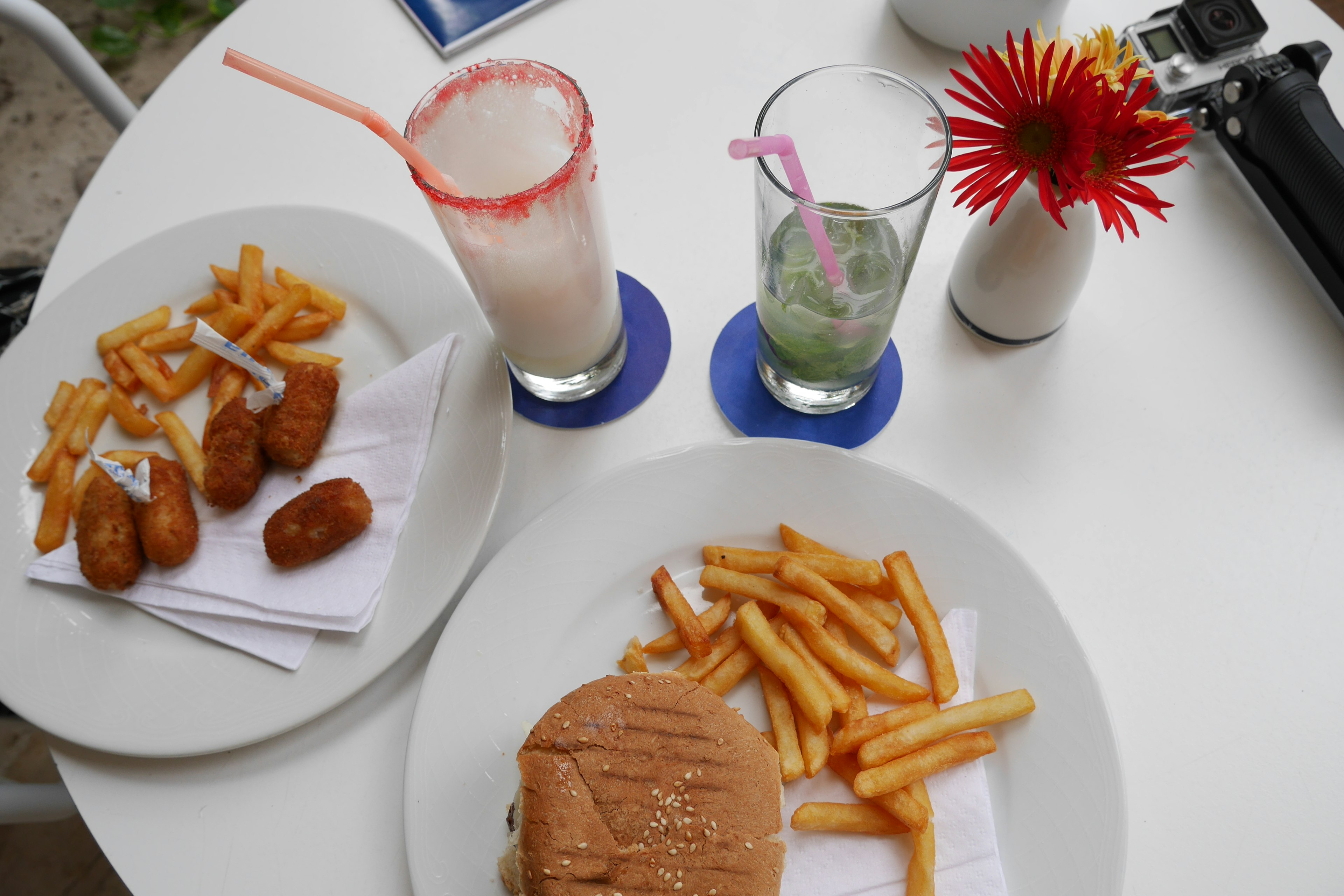 Una mesa con una hamburguesa y papas fritas junto a dos bebidas coloridas