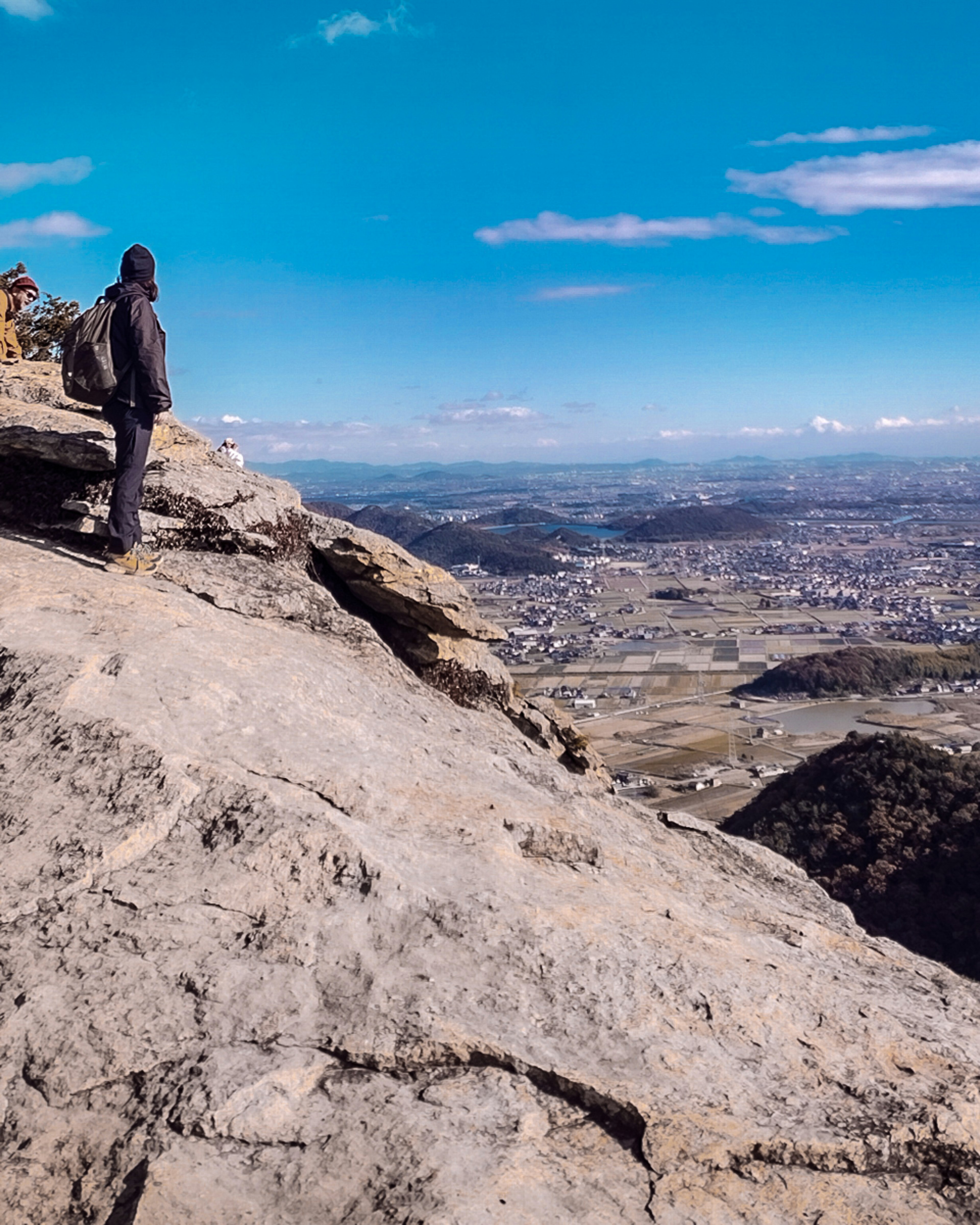 Person steht auf einer felsigen Klippe mit Blick auf eine weite Landschaft