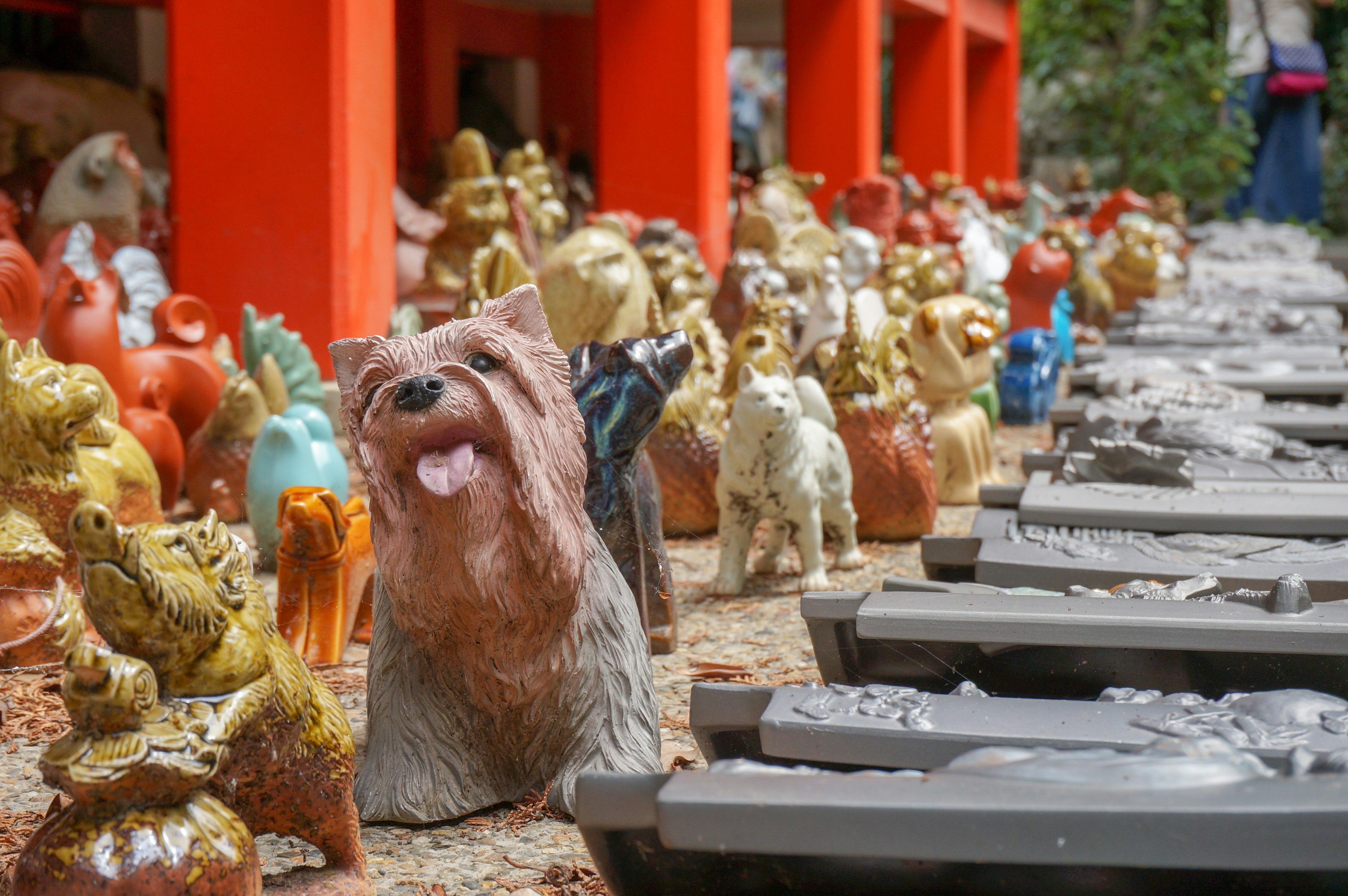 色とりどりの陶器の動物たちが並ぶ風景 中央には犬の像があり 背景にはオレンジ色の柱が見える