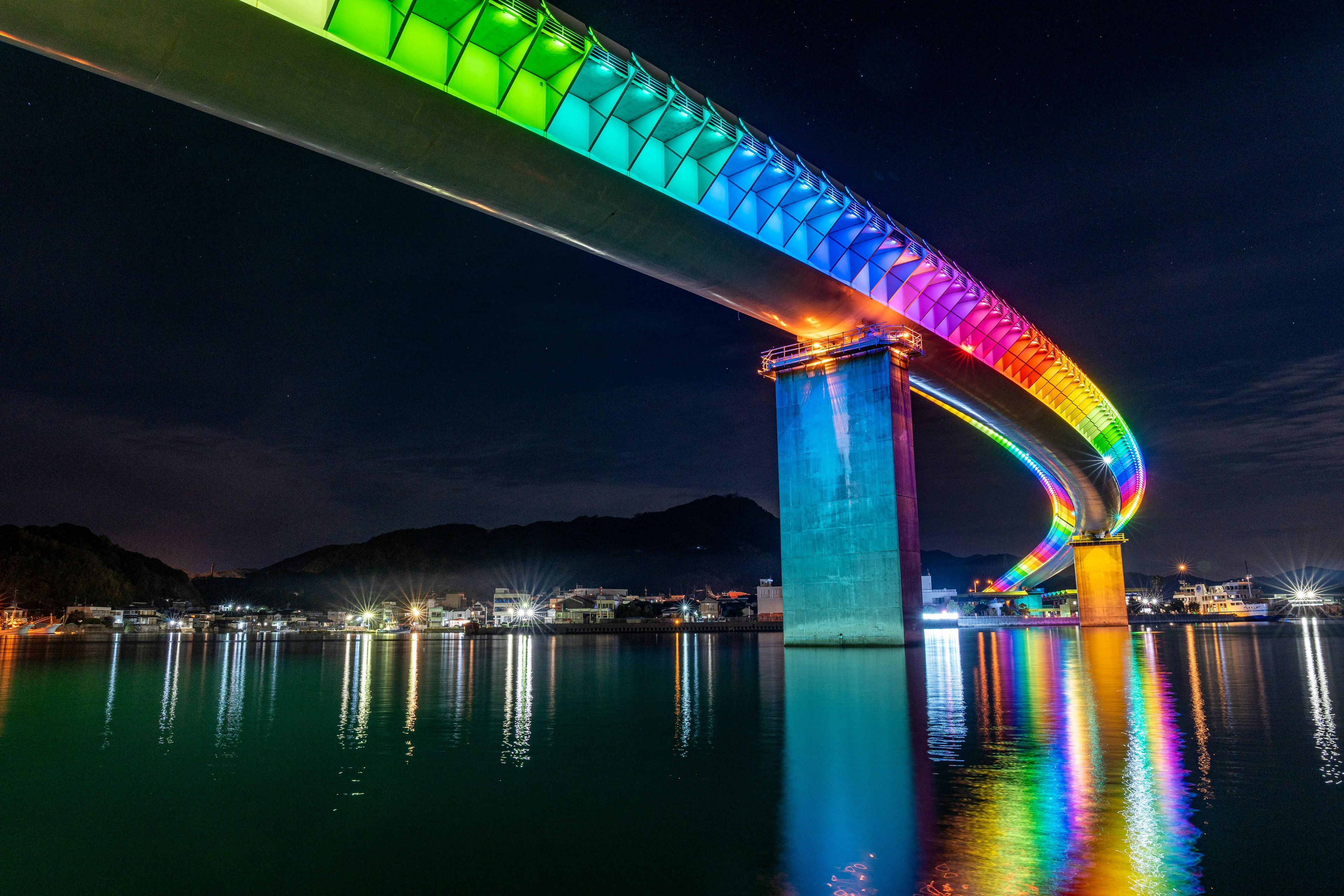 A stunning view of a rainbow-colored bridge reflecting on the water at night