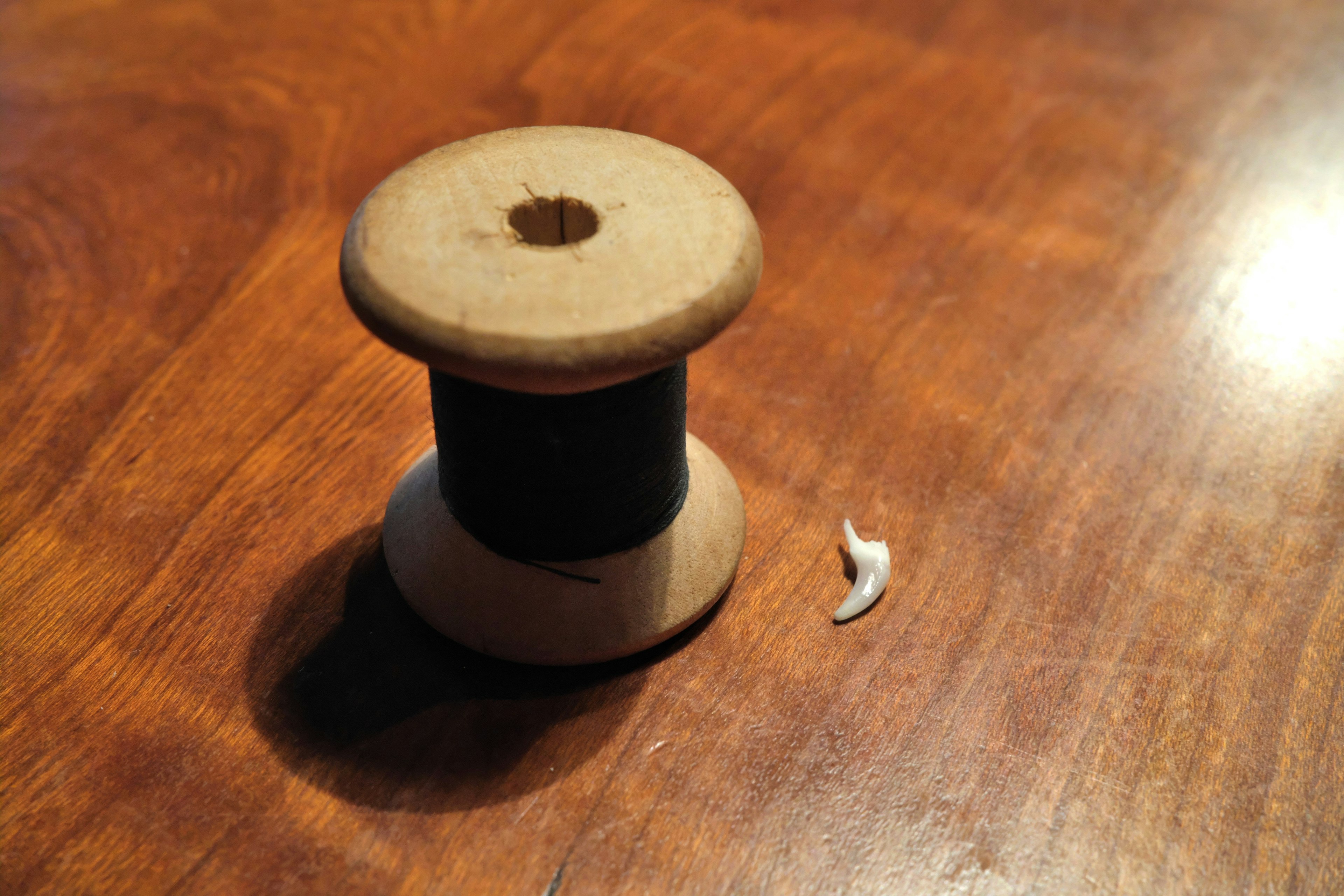 Una bobina de madera con hilo negro y un pequeño trozo blanco sobre una mesa de madera