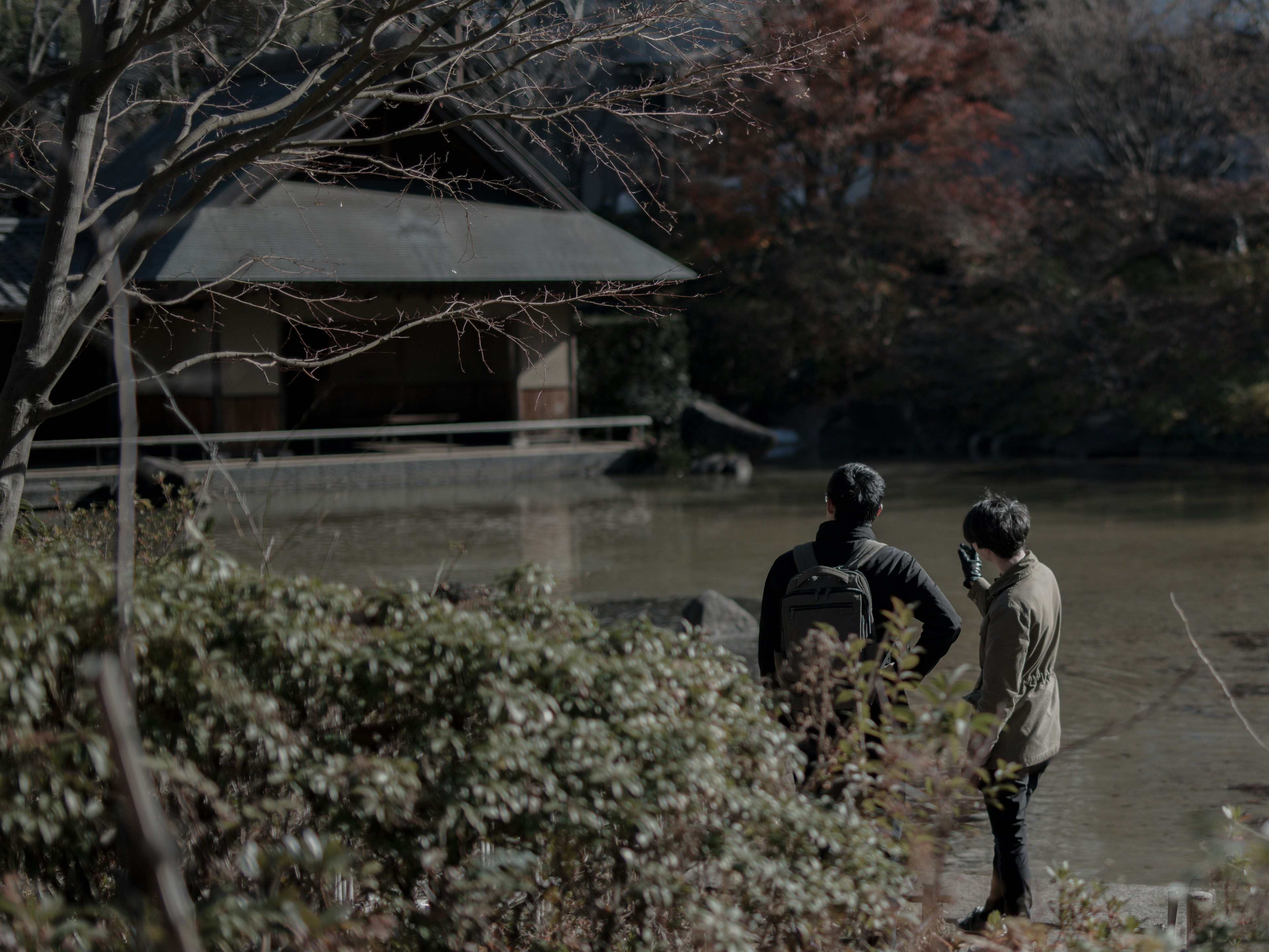 池の近くで話している二人の男性と紅葉した木々