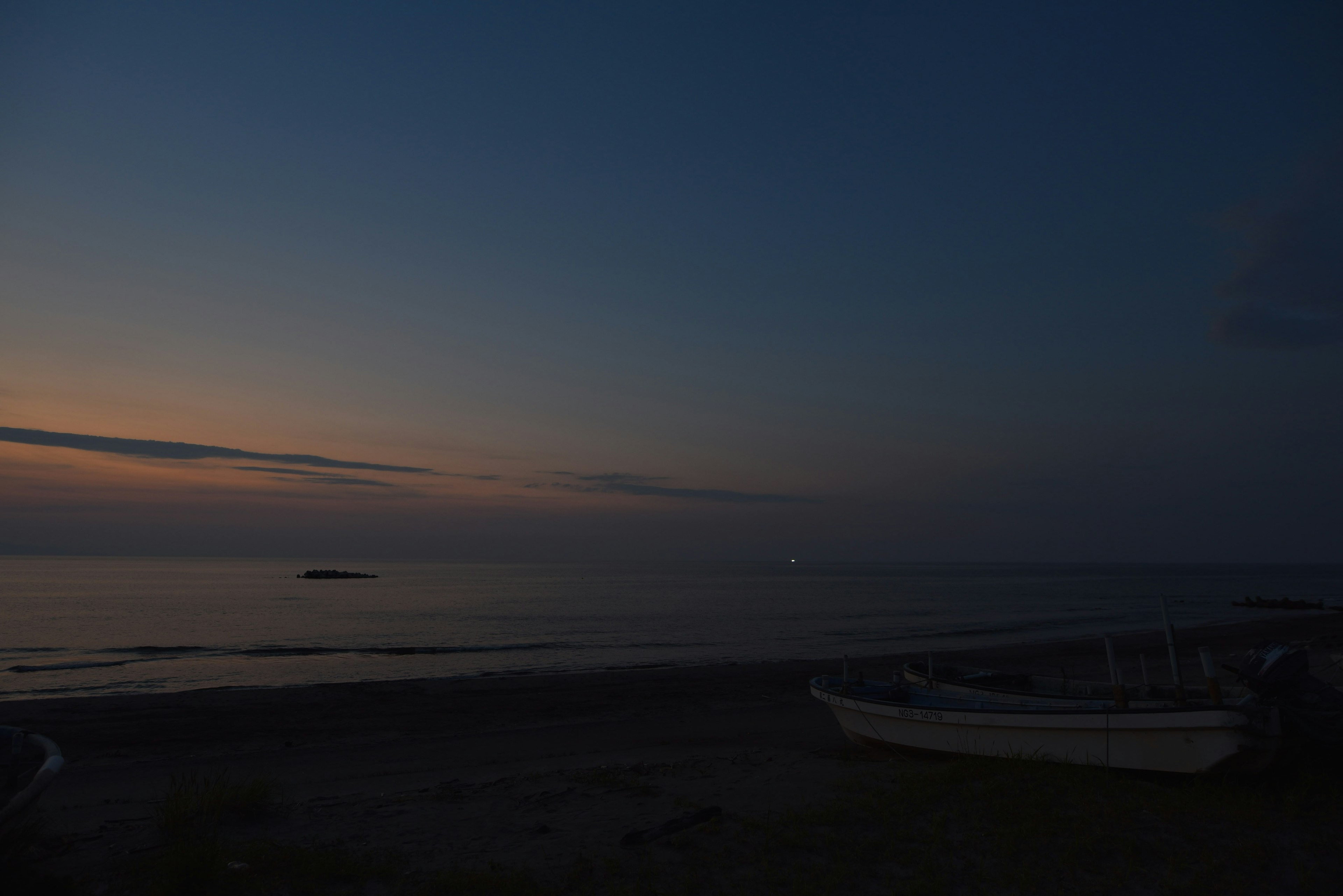 Küstenansicht bei Dämmerung mit ruhigem Meer und fernen Lichtern